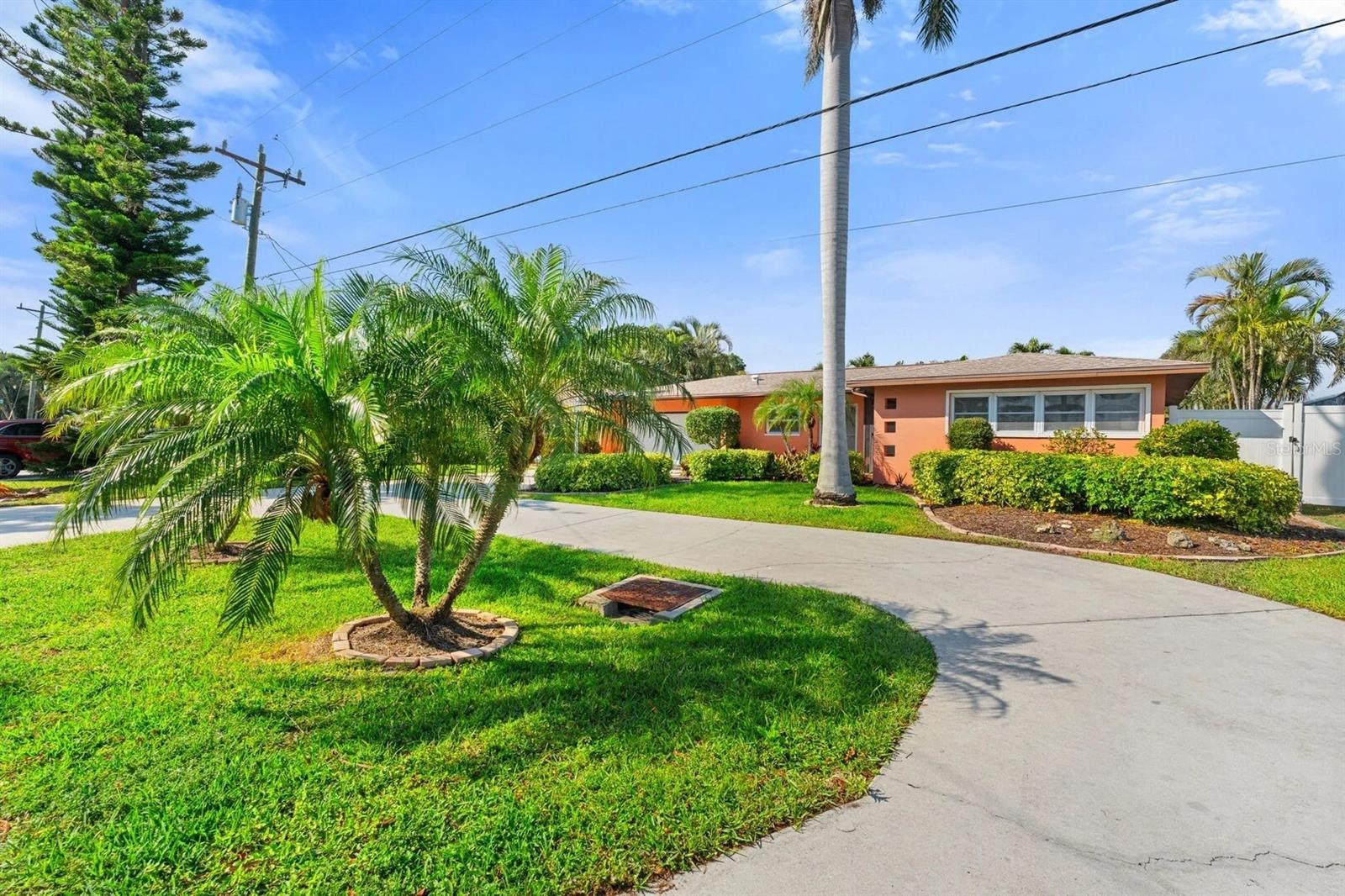 Coral single-story home with a curved driveway, palm trees, and landscaped front yard.