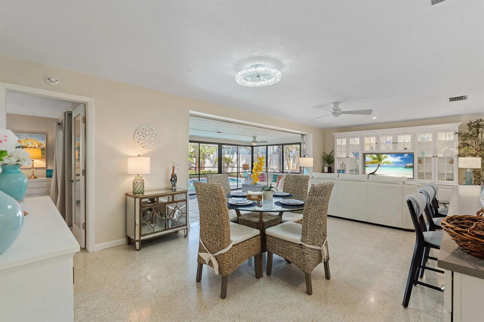 Dining and living area with wicker chairs, white built-ins, and a screened lanai overlooking the pool.