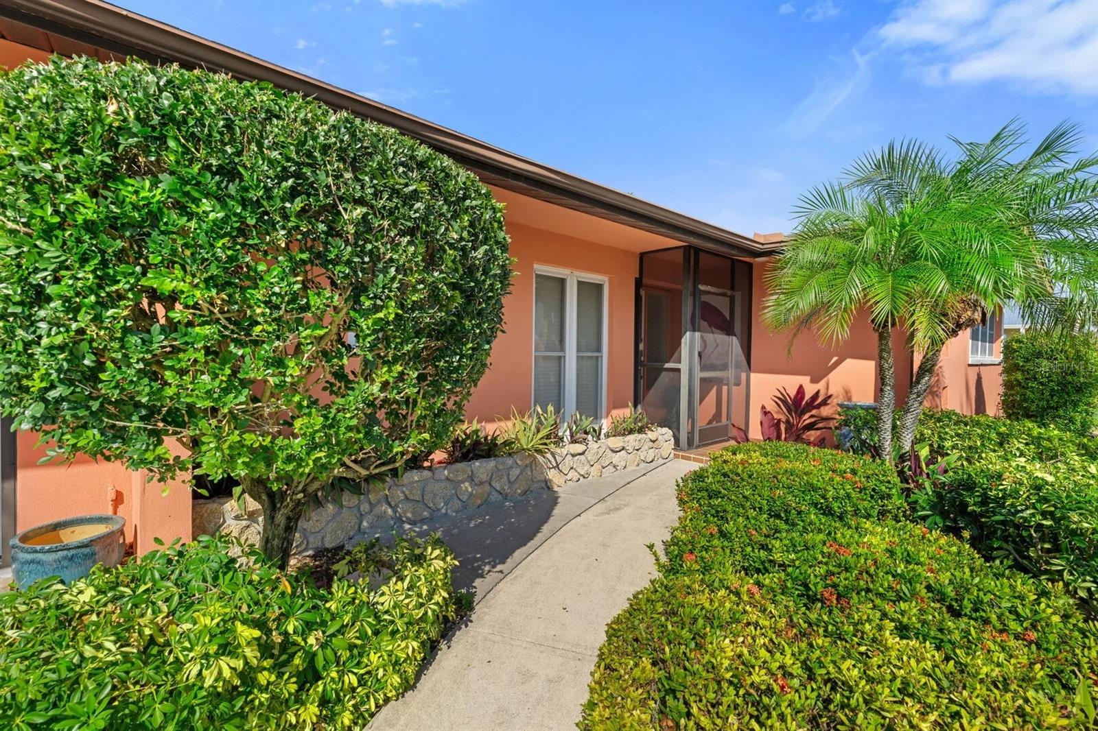 Coral stucco home with a screened entry, curved walkway, and lush tropical landscaping.