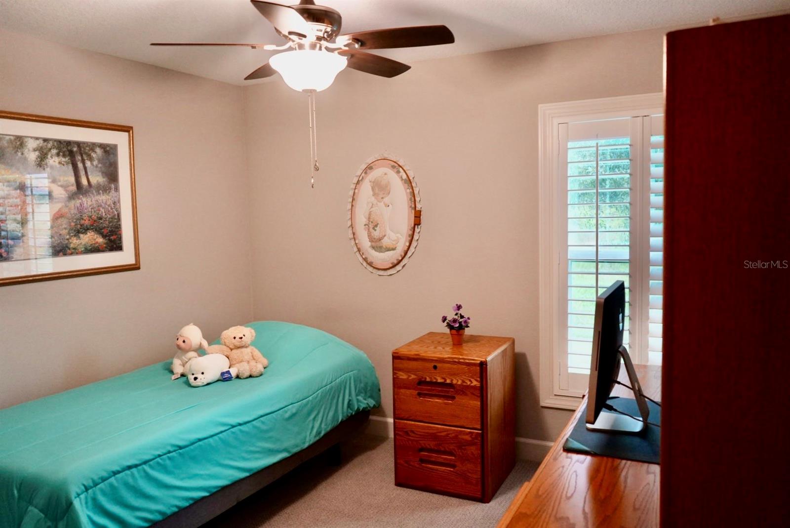 Bedroom with a turquoise single bed, stuffed animals, wooden dresser, and shuttered glass door.