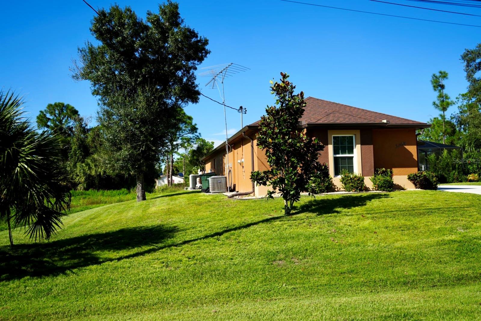 Single-story tan stucco home with a brown roof, screened lanai, and broad green lawn.