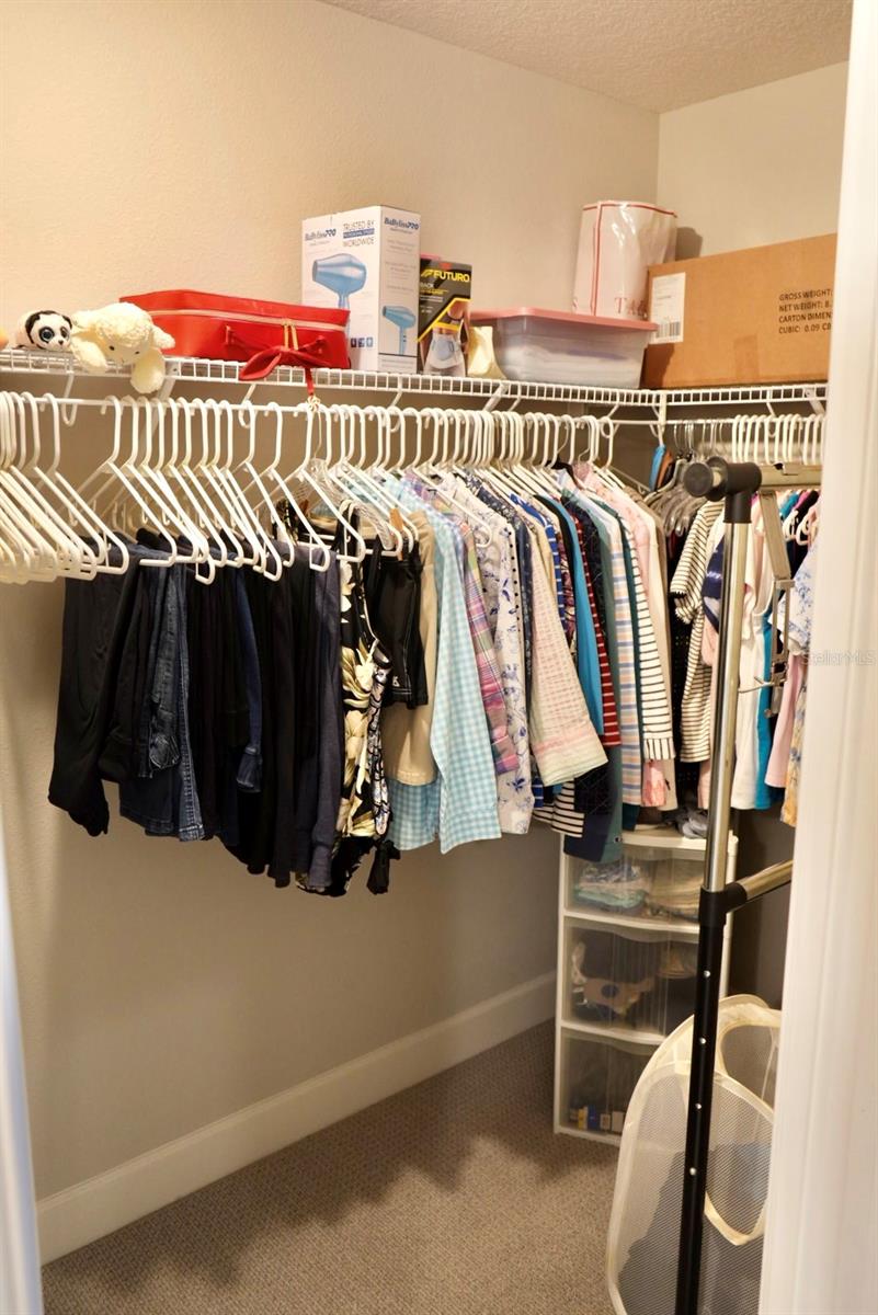 Walk-in closet with clothes on white wire racks, storage bins above, and plastic drawers in the corner.