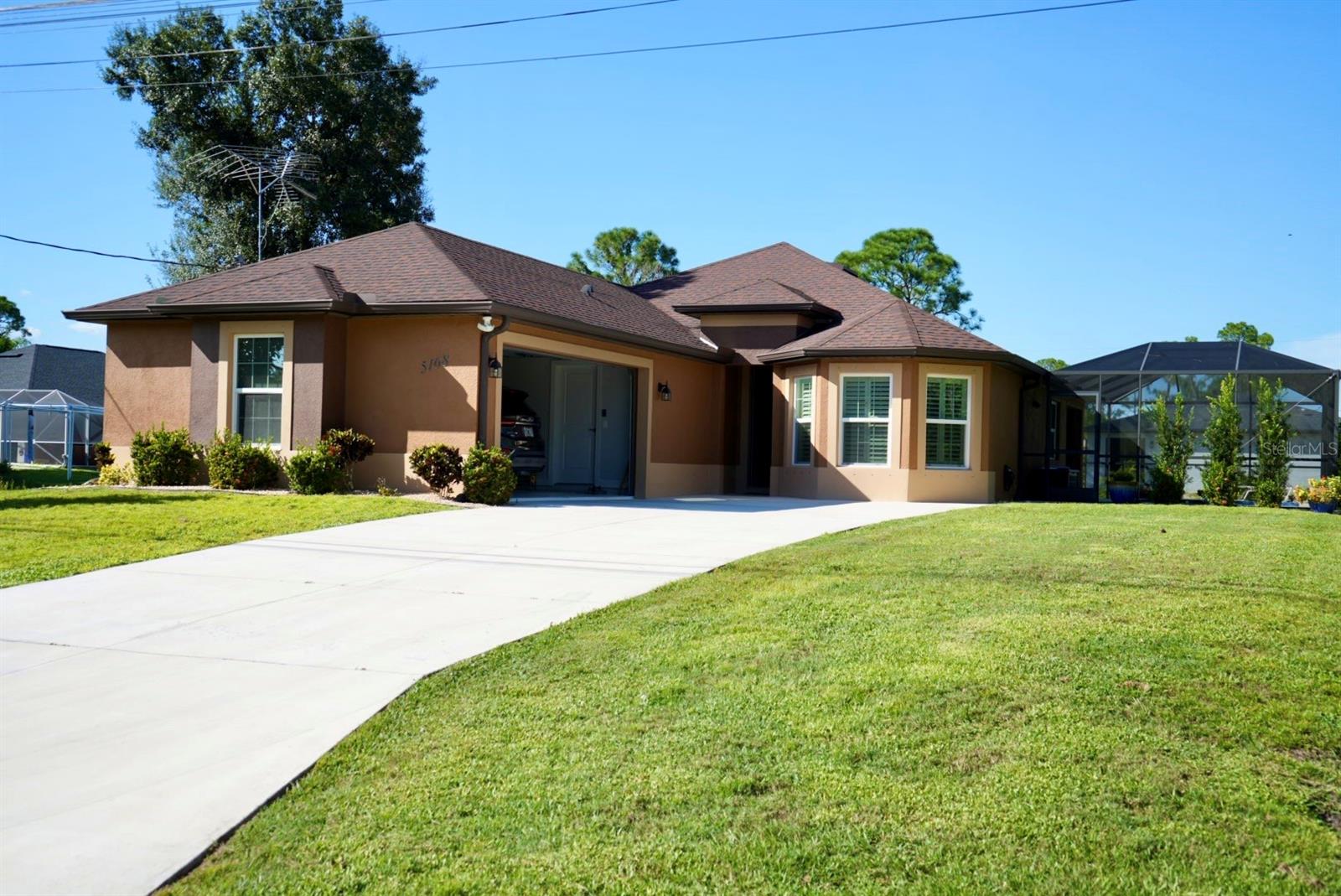 Tan stucco home with a broad driveway, green lawn, and screened lanai.