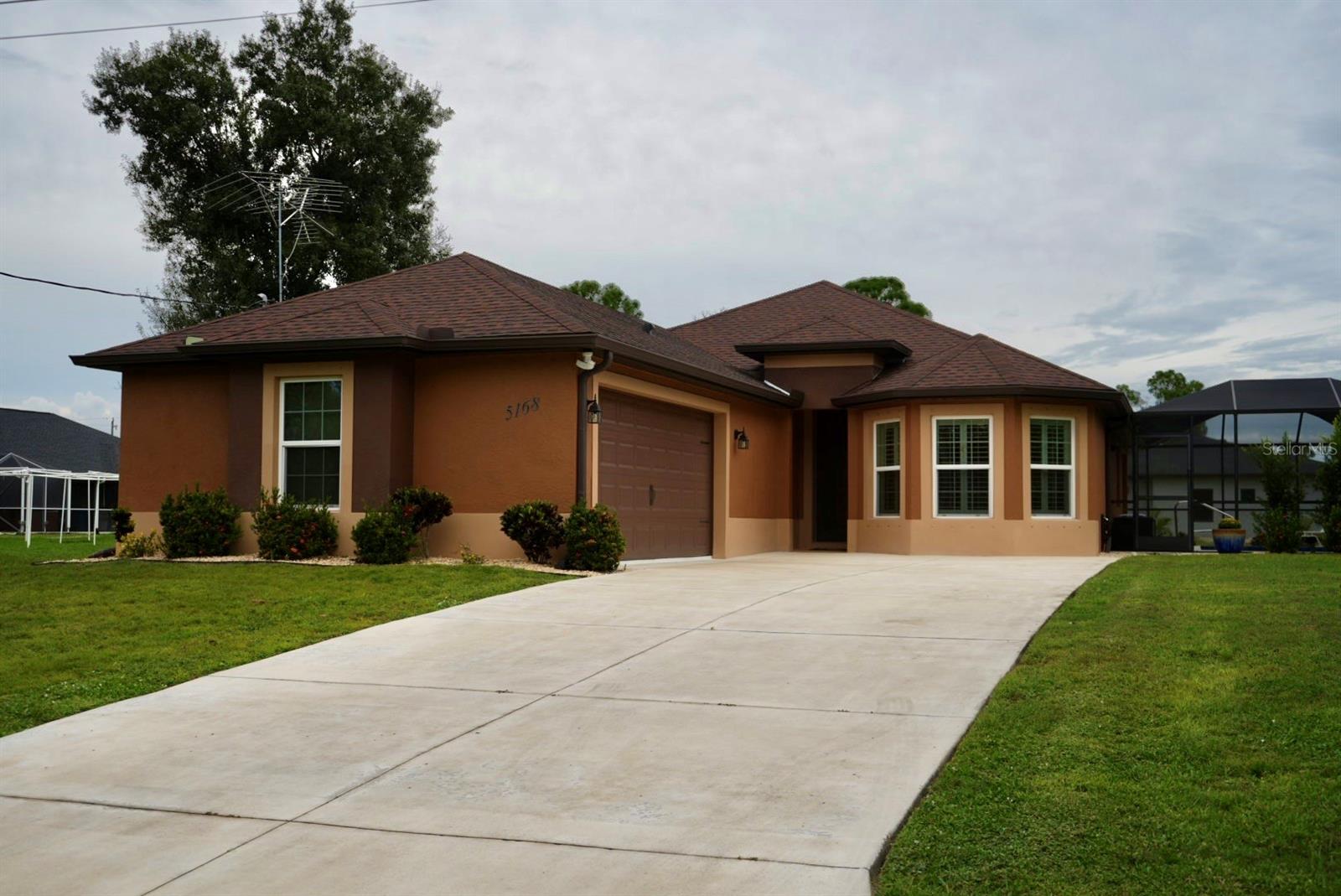 Brown stucco house with attached garage, wide concrete driveway, and screened lanai.