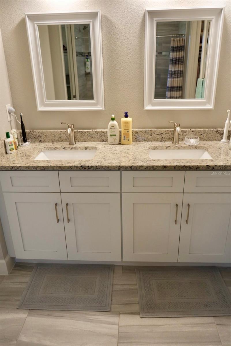 Bathroom double vanity with speckled stone countertop, white cabinets, and two framed mirrors.