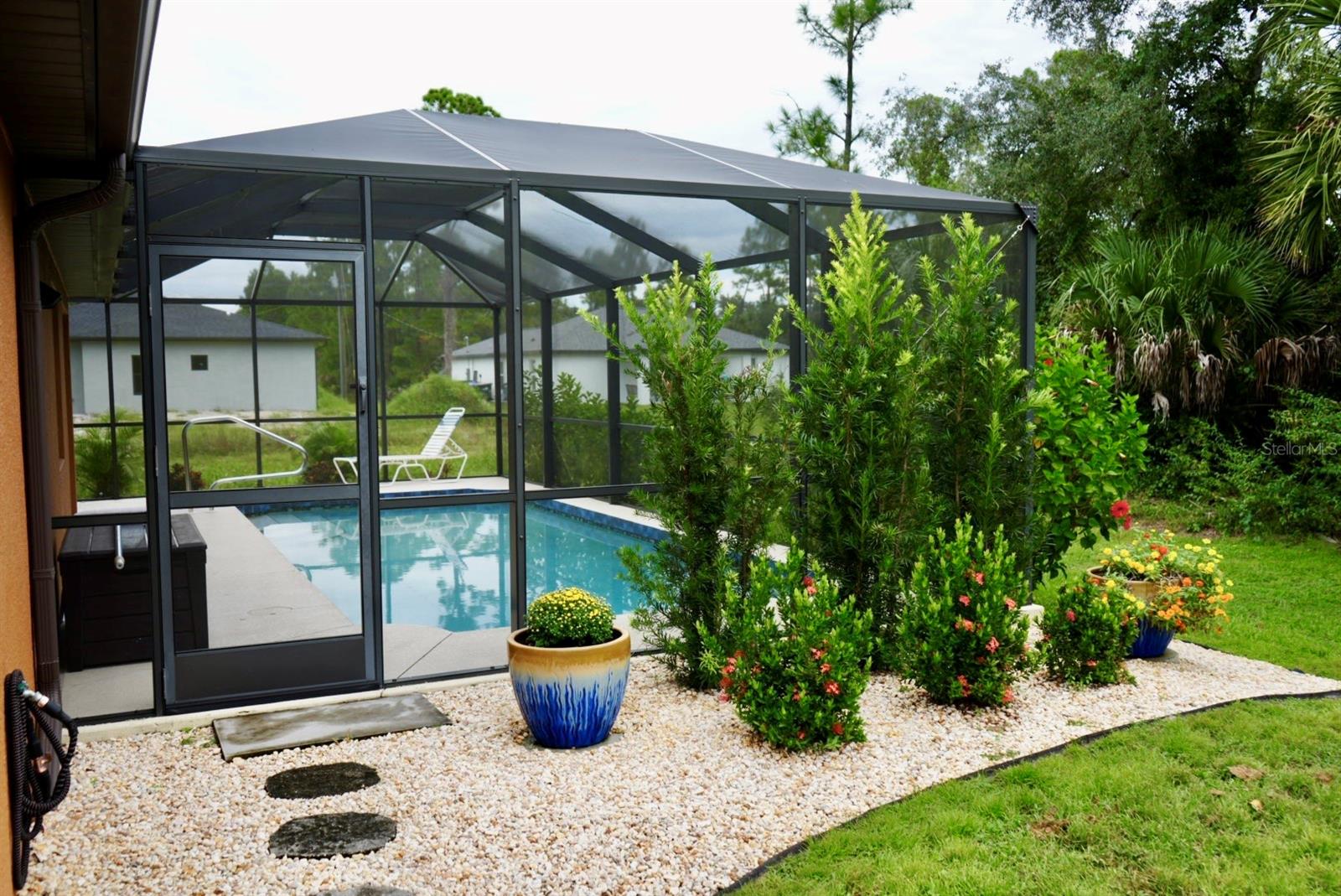 Screened backyard pool with a lounge chair and flowering garden beds.