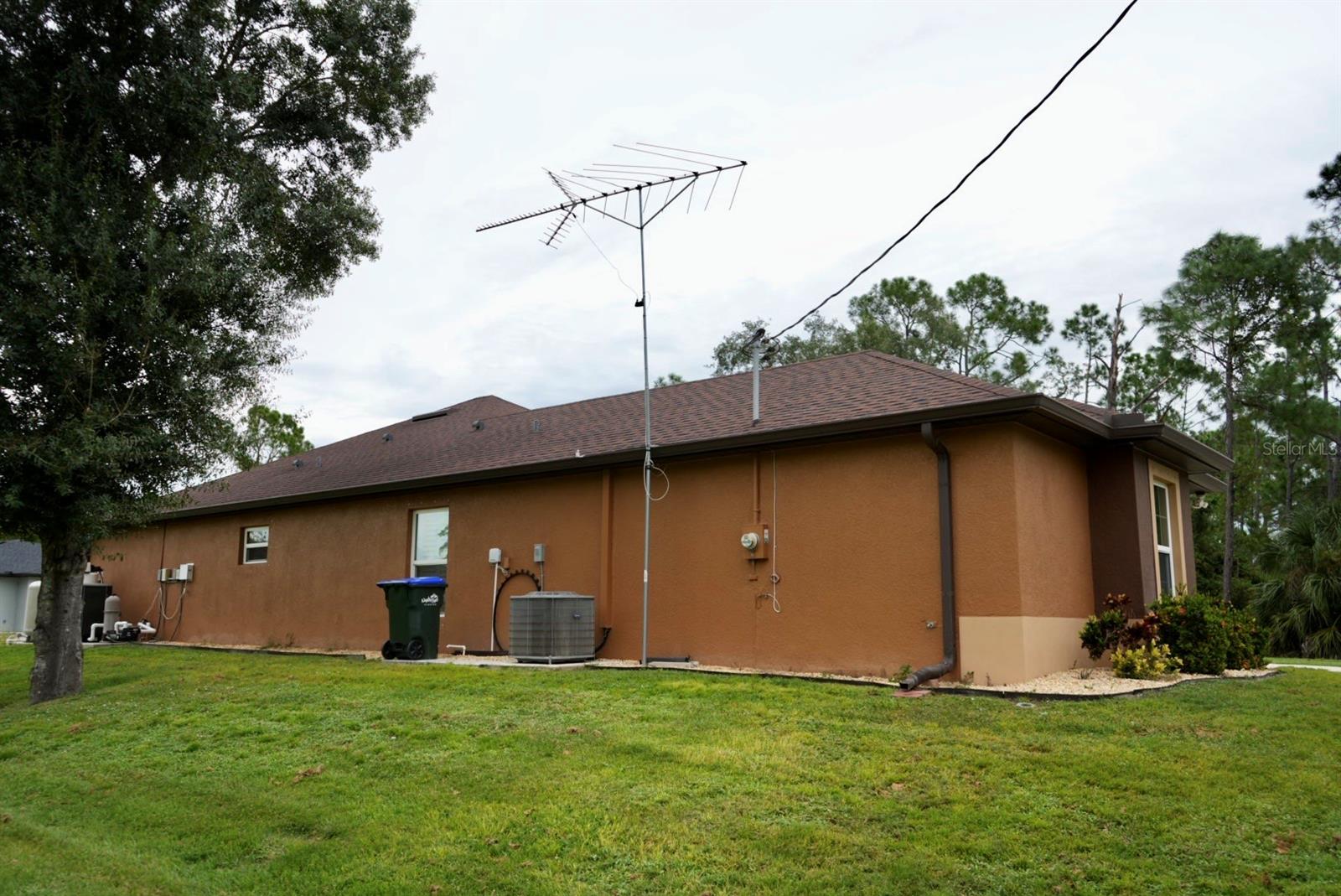 Side exterior of a brown single-story home with a rooftop antenna and broad lawn.