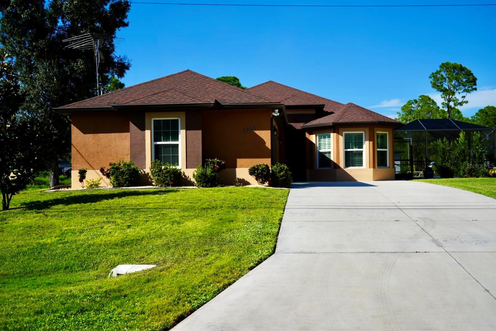 Single-story brown stucco home with a broad driveway, green lawn, and screened pool enclosure.