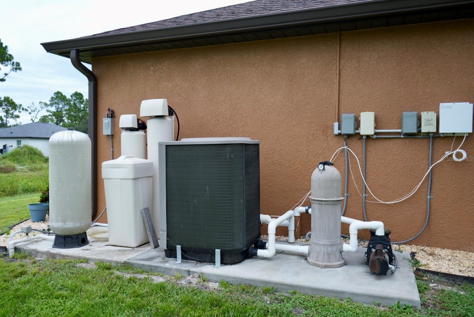 Home exterior with water-treatment tanks, filtration equipment, and an HVAC condenser.