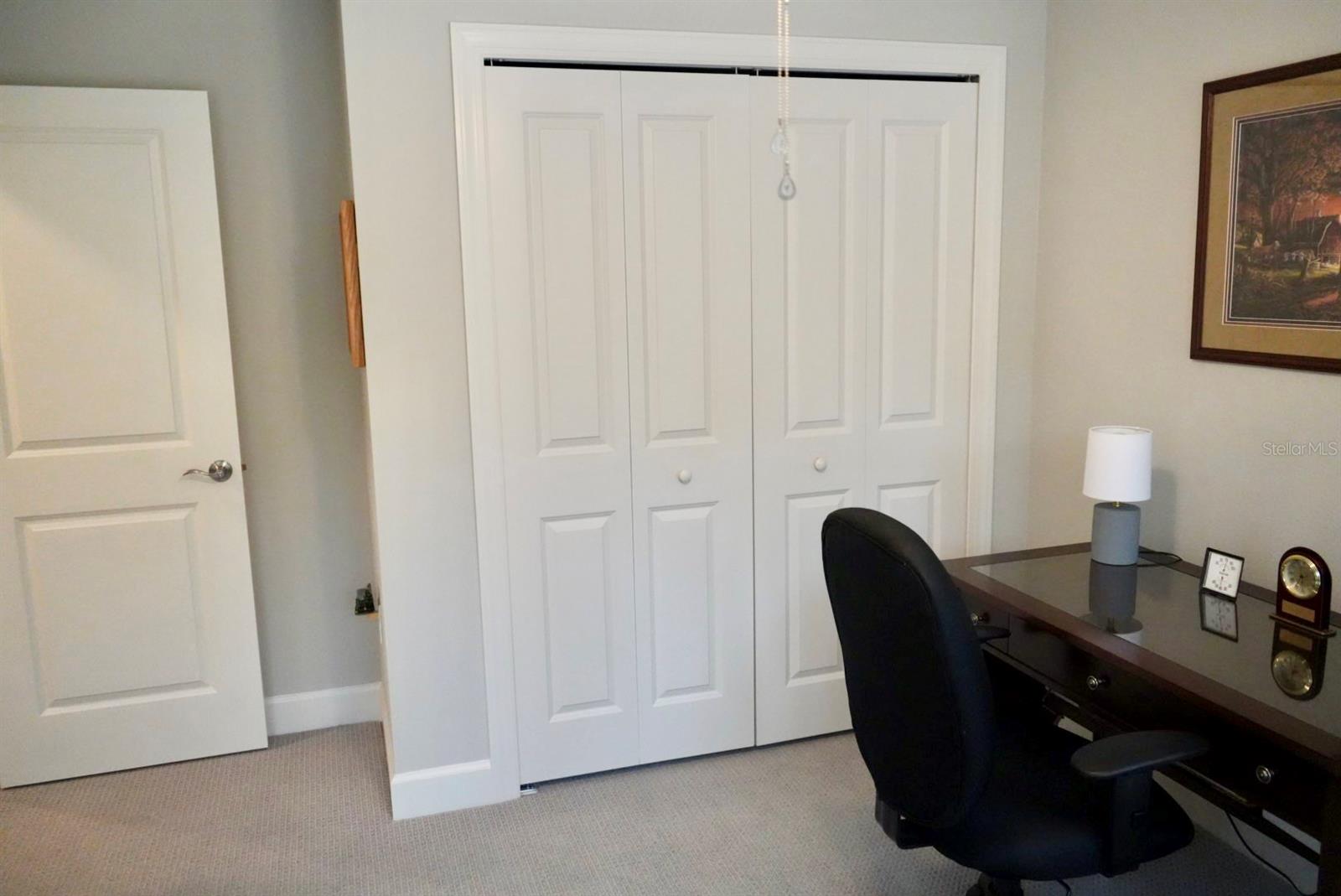 Home office with a dark desk and chair beside white paneled closet doors.