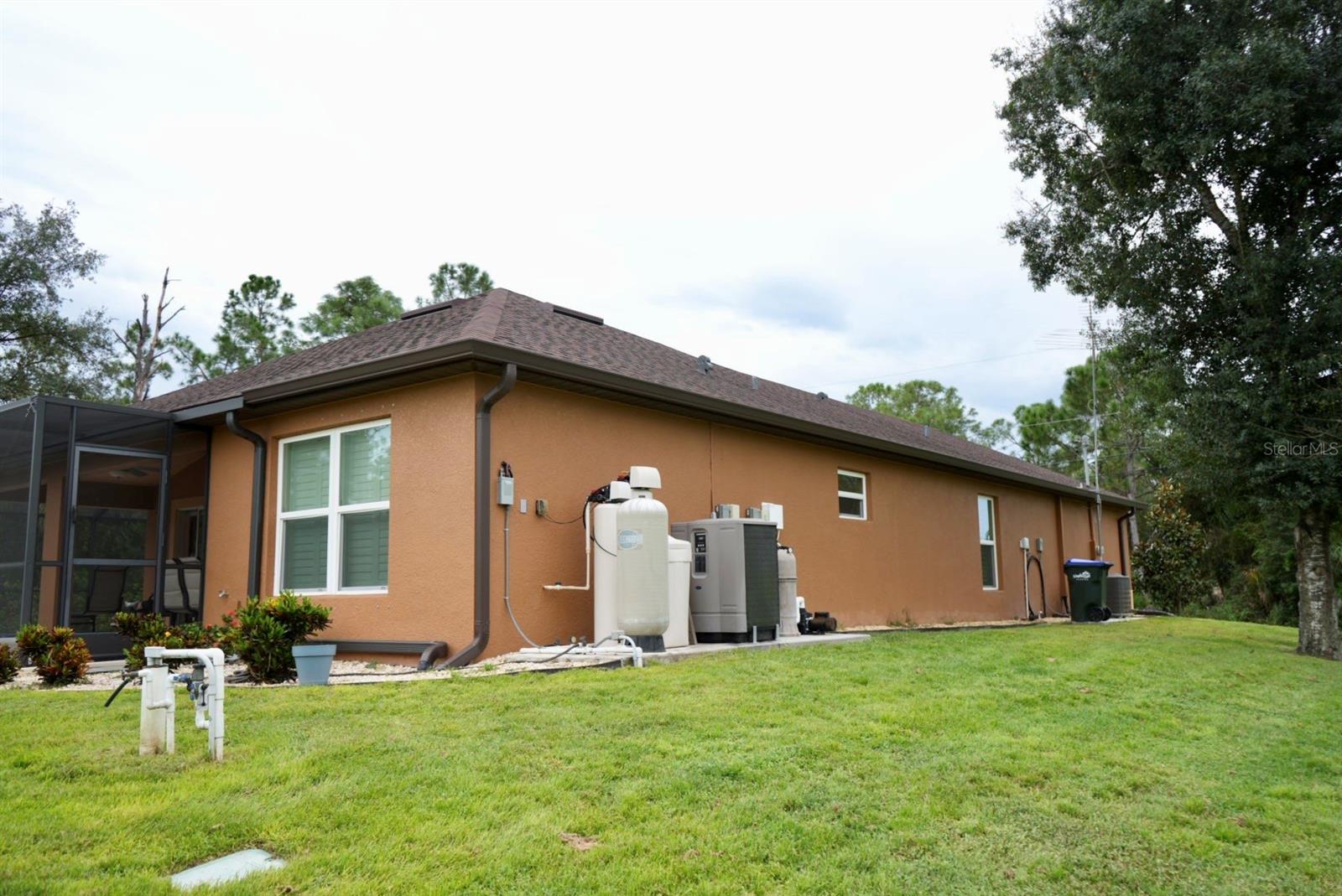 Rear exterior with tan stucco, screened lanai, and outdoor utility equipment.