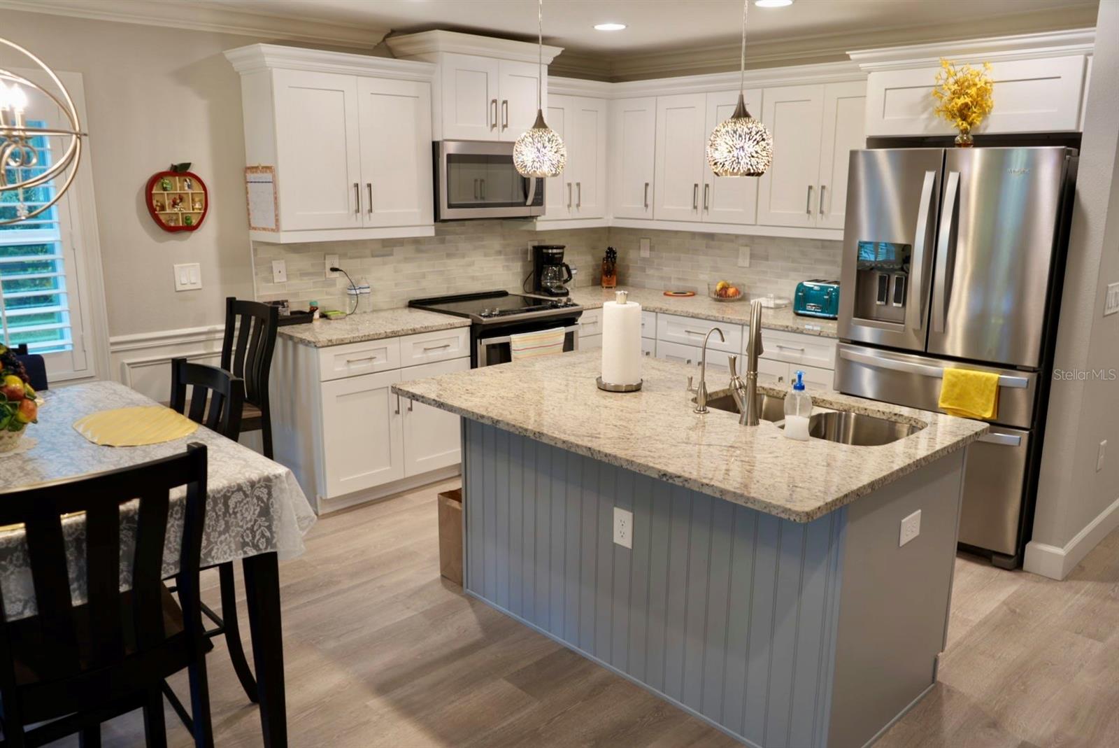 Kitchen with white cabinetry, stainless steel appliances, and a large island with a double sink.