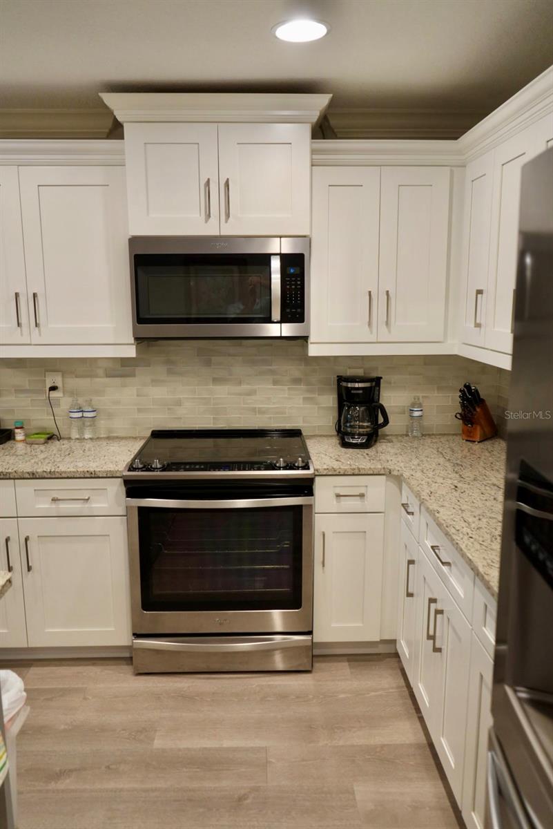 Kitchen with white cabinets, granite counters, tiled backsplash, and stainless-steel appliances.
