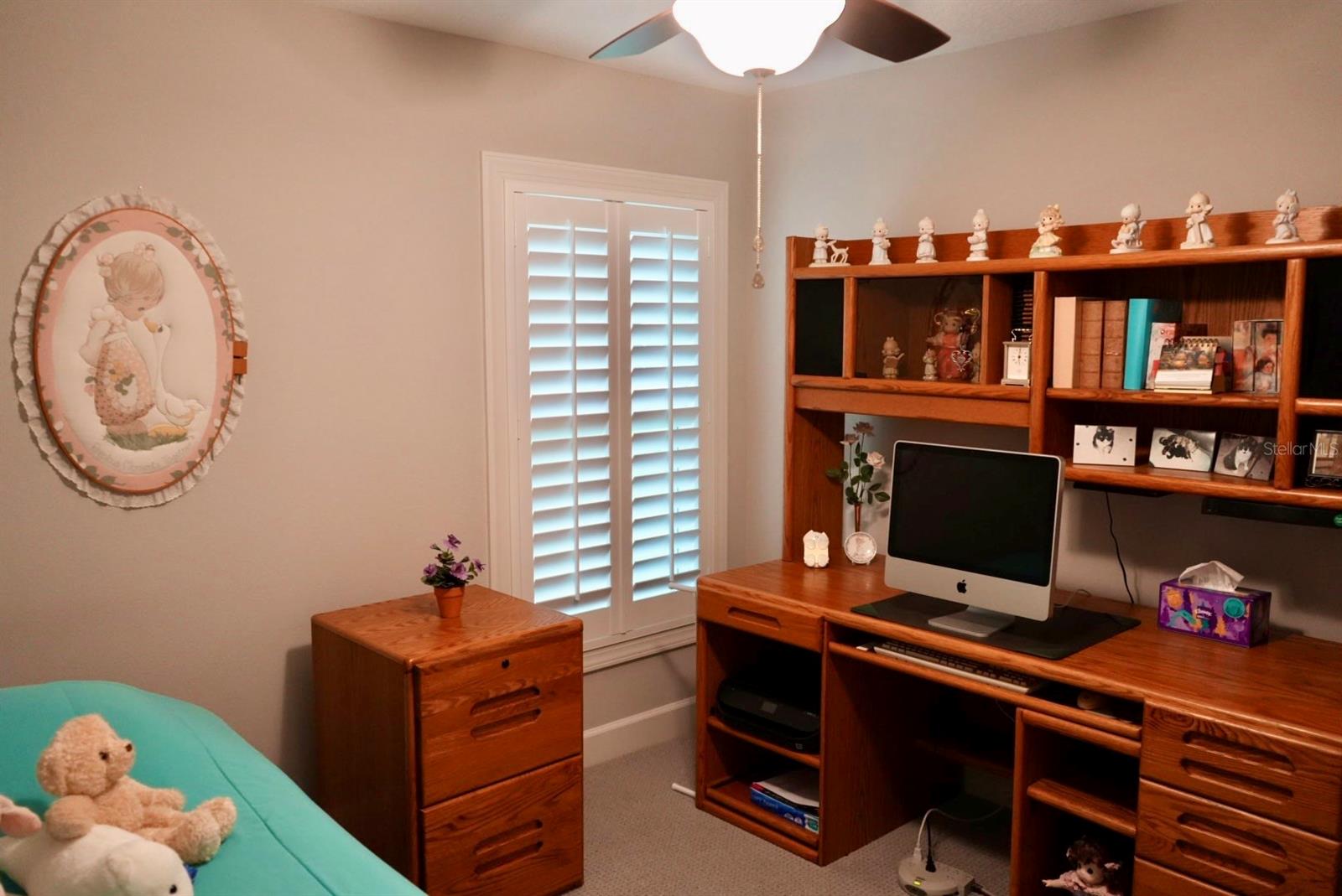 Bedroom office with a wooden desk and shelves beside shuttered windows and a turquoise bed.