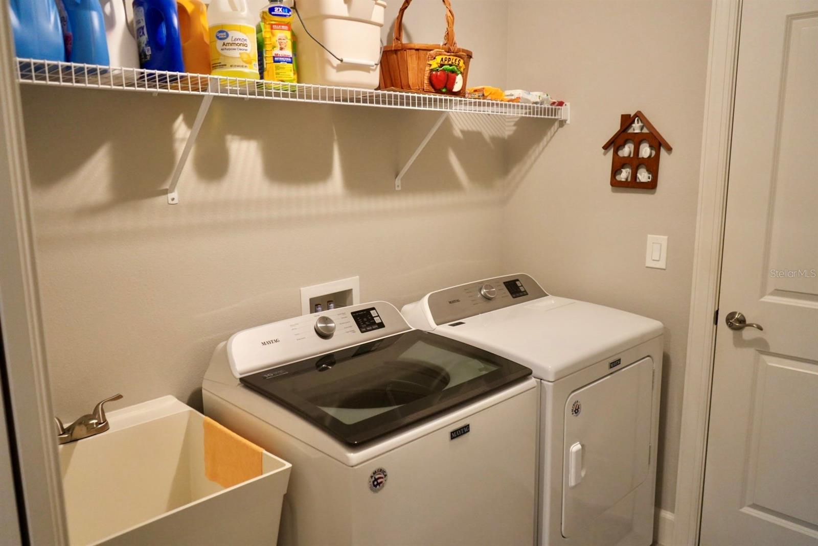 Laundry room with a Maytag washer and dryer, deep utility sink, and supply shelf.