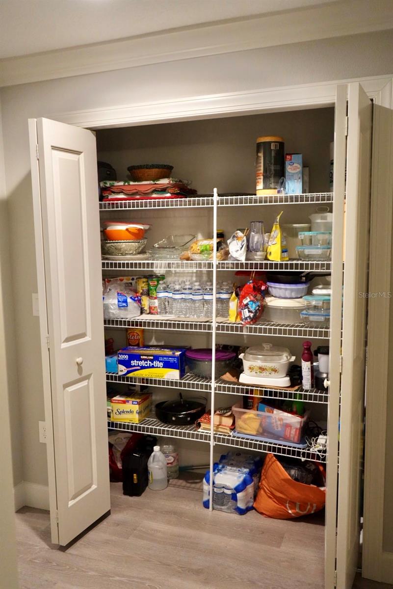 Open pantry closet with stocked wire shelves and double white doors.