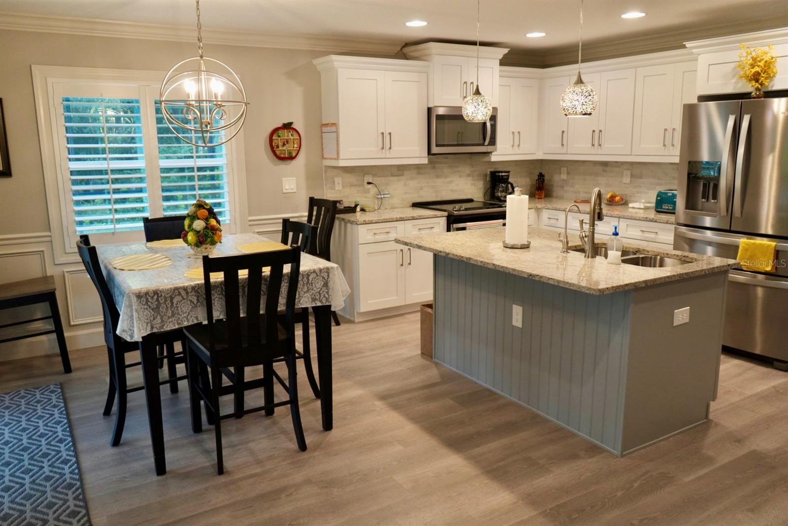 Kitchen and dining area with a large gray island, white cabinets, and stainless steel appliances.