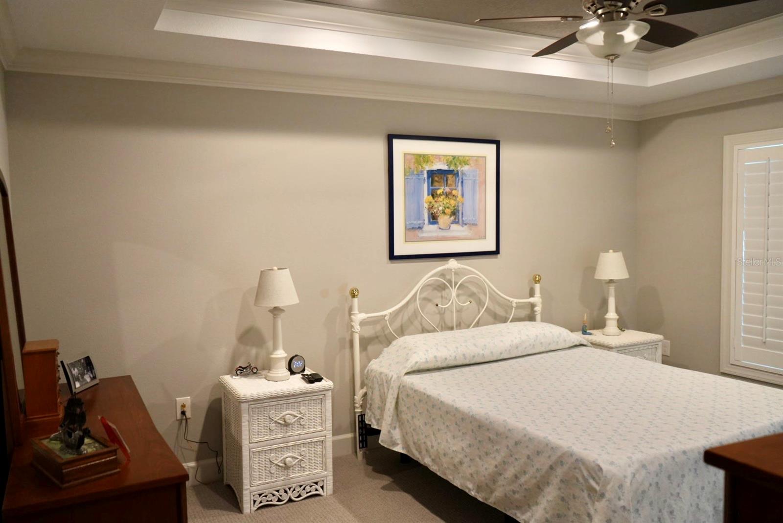 Bedroom with a white metal bed, floral bedding, matching wicker nightstands, and a tray ceiling.