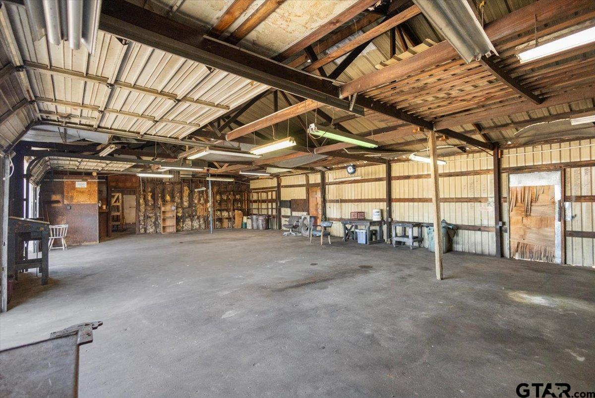 Large metal workshop with exposed roof trusses, a broad concrete floor, and workbenches along the walls.