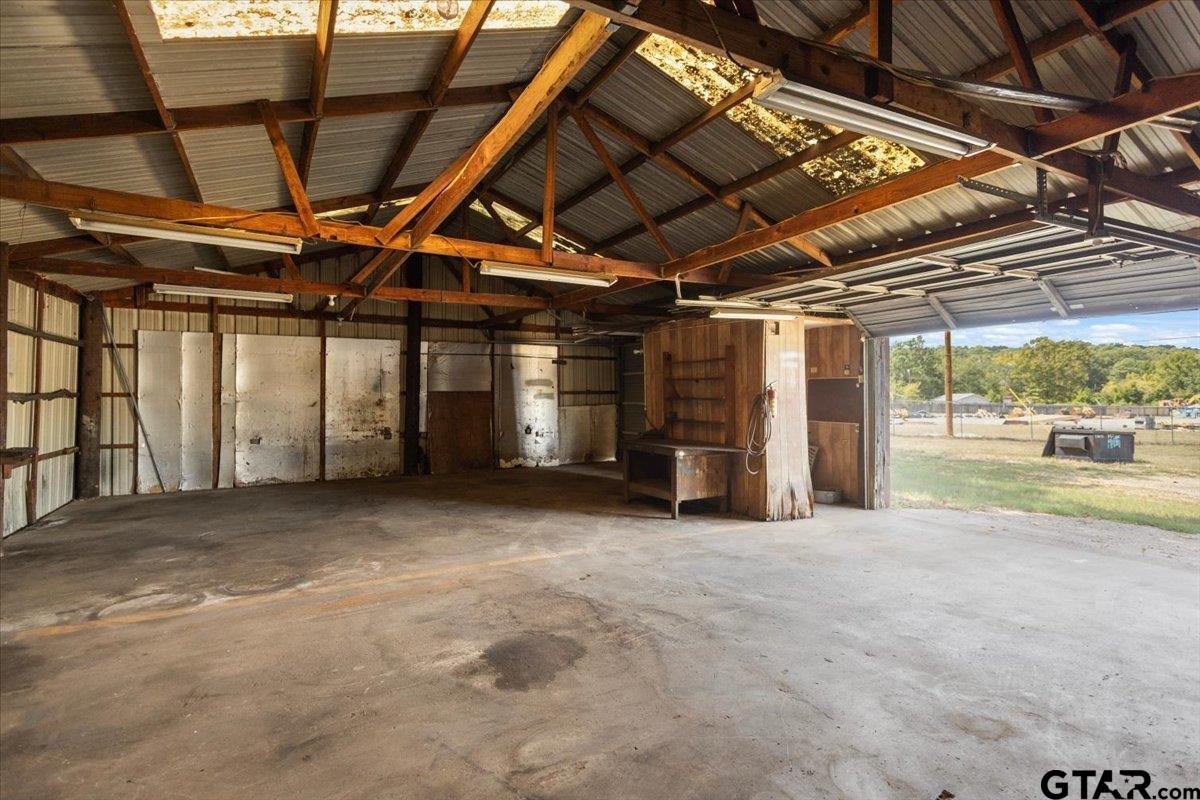 Large garage interior with exposed wooden trusses, concrete floor, and open garage door.