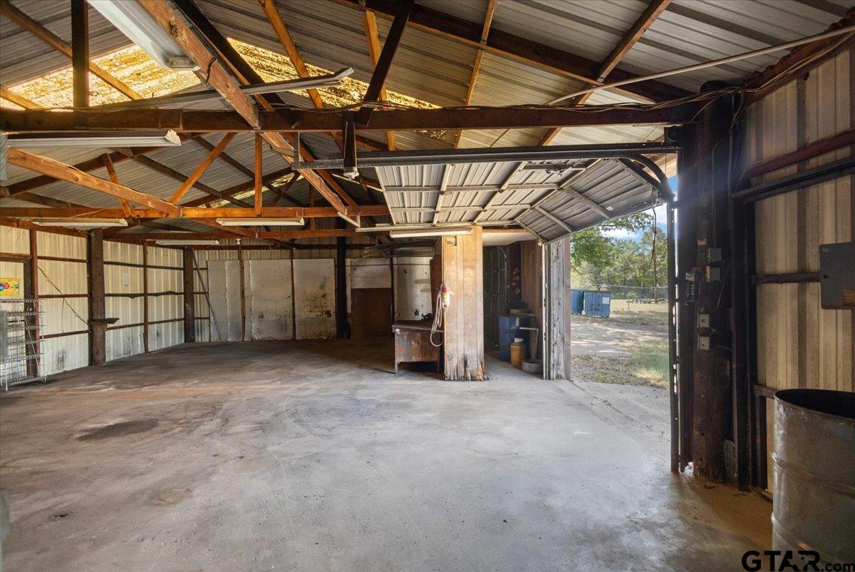 Metal workshop interior with exposed wooden trusses, concrete floor, and an open garage door.