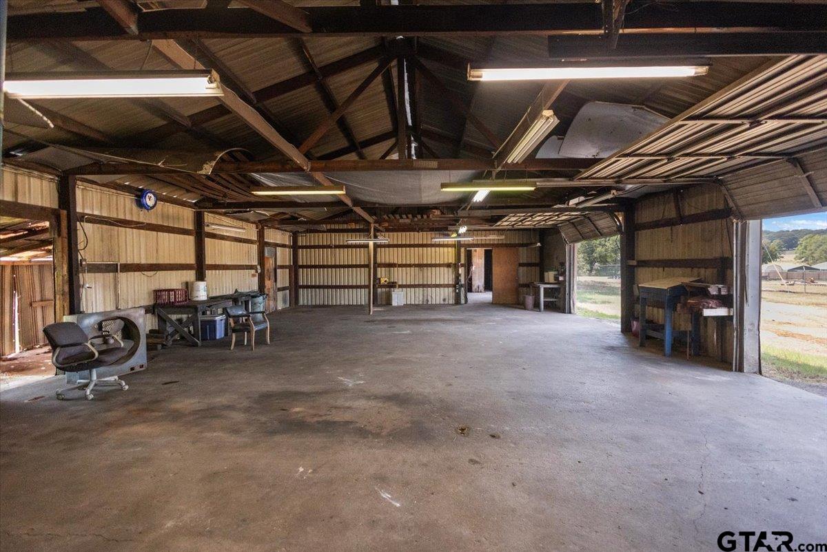 Spacious metal workshop with exposed roof trusses, concrete floor, workbenches, and open bays.