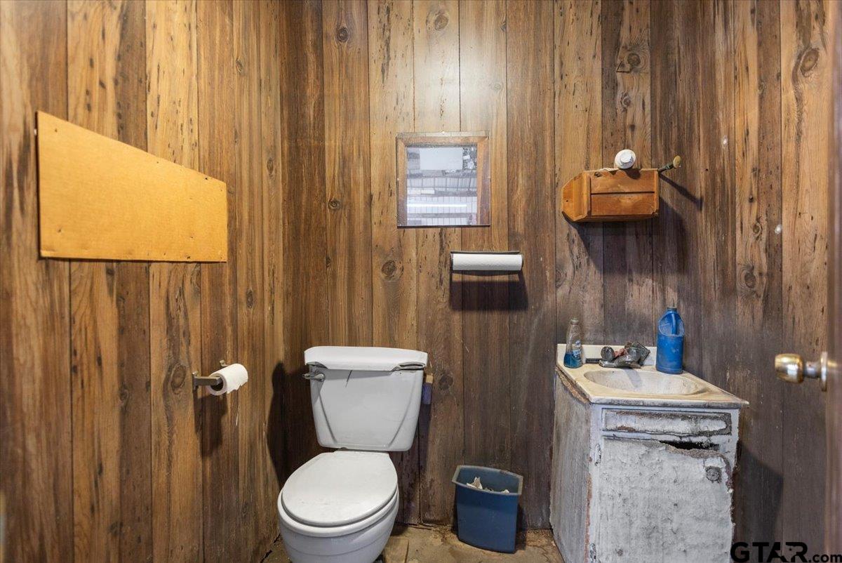Bathroom with wood-paneled walls, a white toilet, and a distressed sink cabinet.