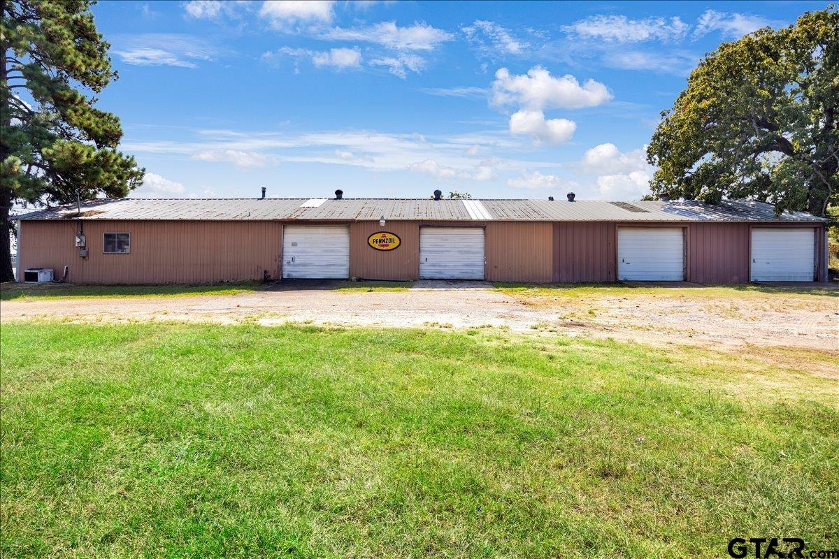 Long brown metal garage building with four white roll-up doors and a Pennzoil sign.