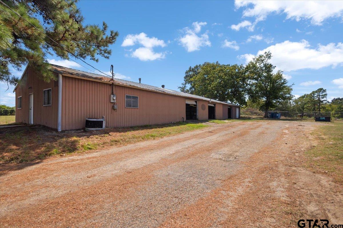 Long brown metal-sided building with multiple open bays beside a broad gravel driveway.