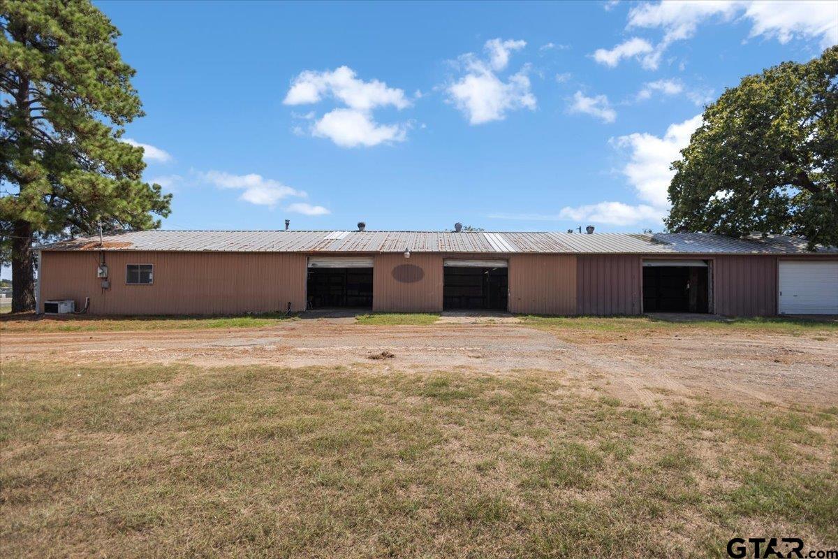 Long metal building with multiple open garage bays beside a dirt and gravel drive.