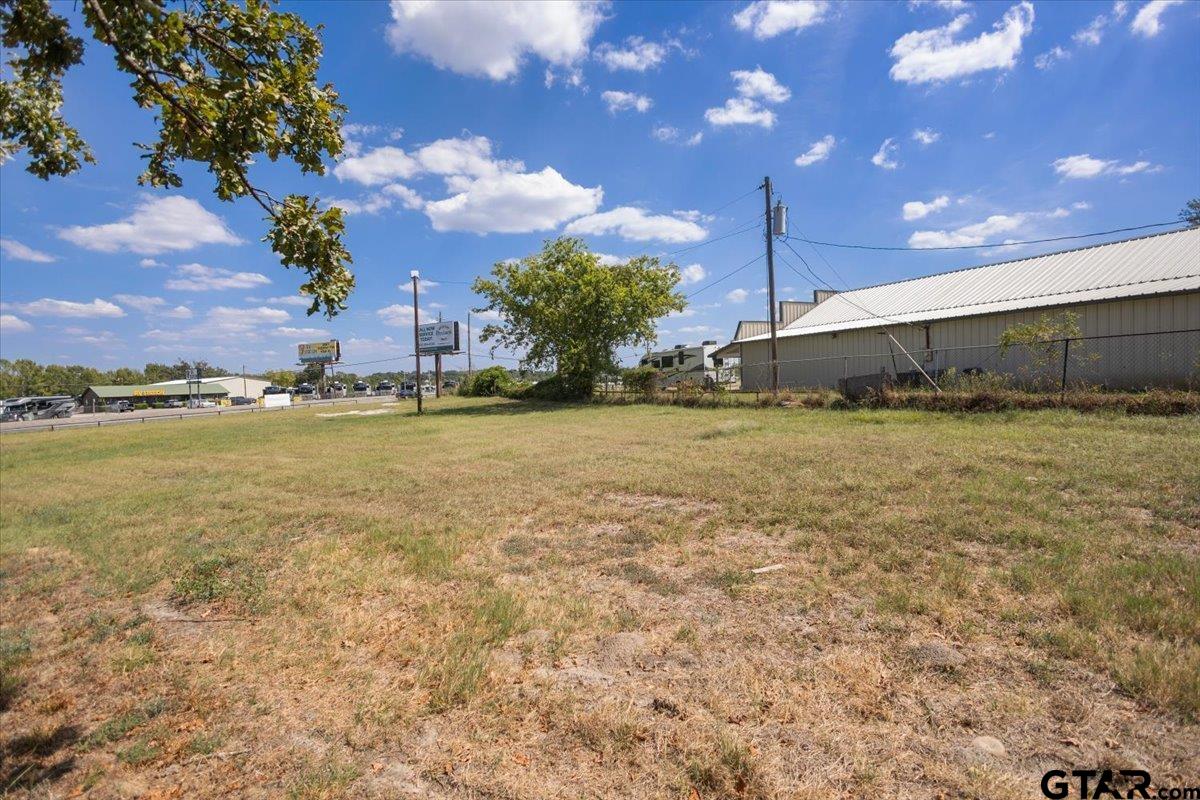 Grassy roadside lot beside a metal-sided building, with businesses in the distance.