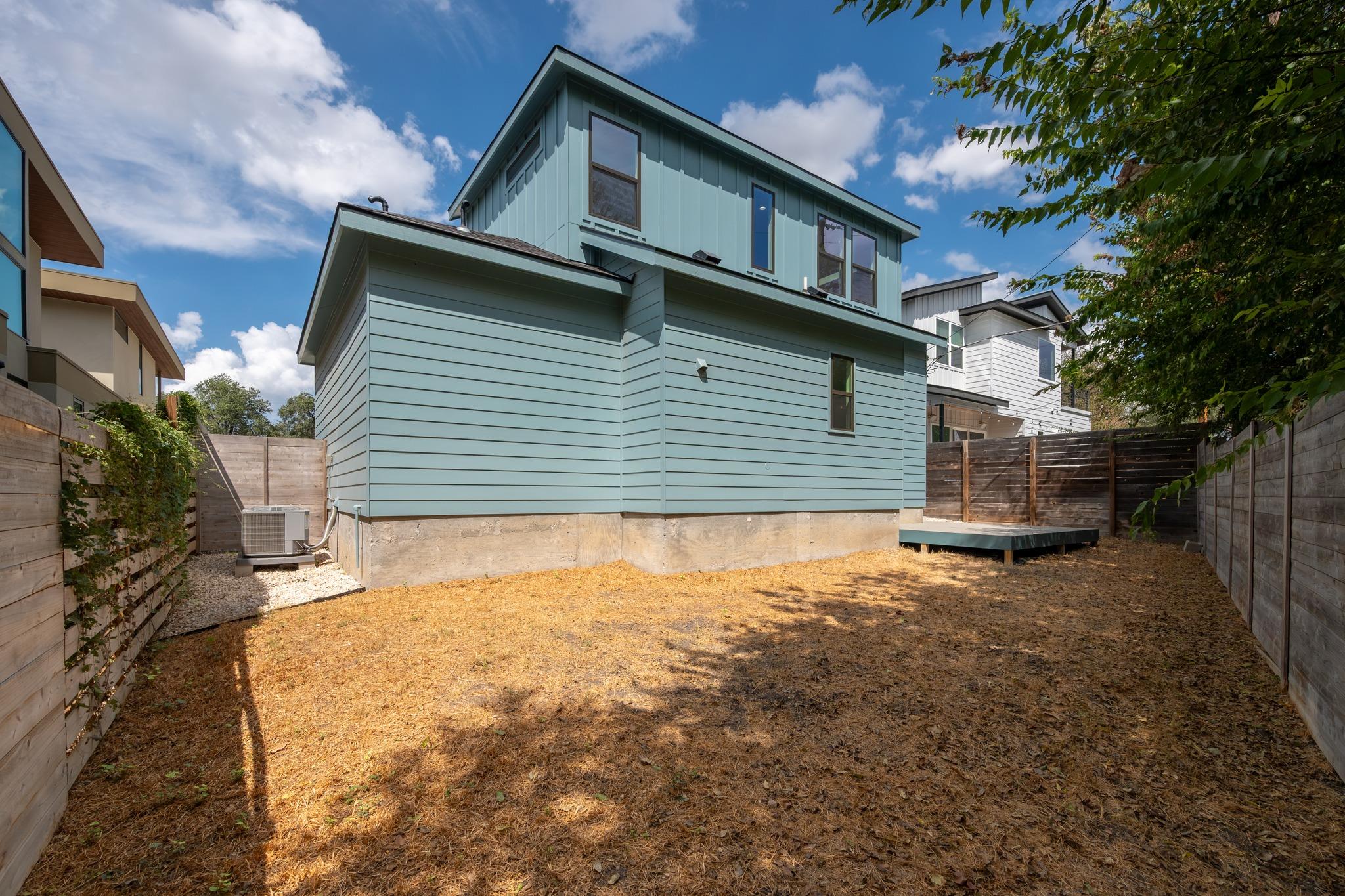 Rear exterior of a blue-sided home with a fenced, dry yard and small raised deck.