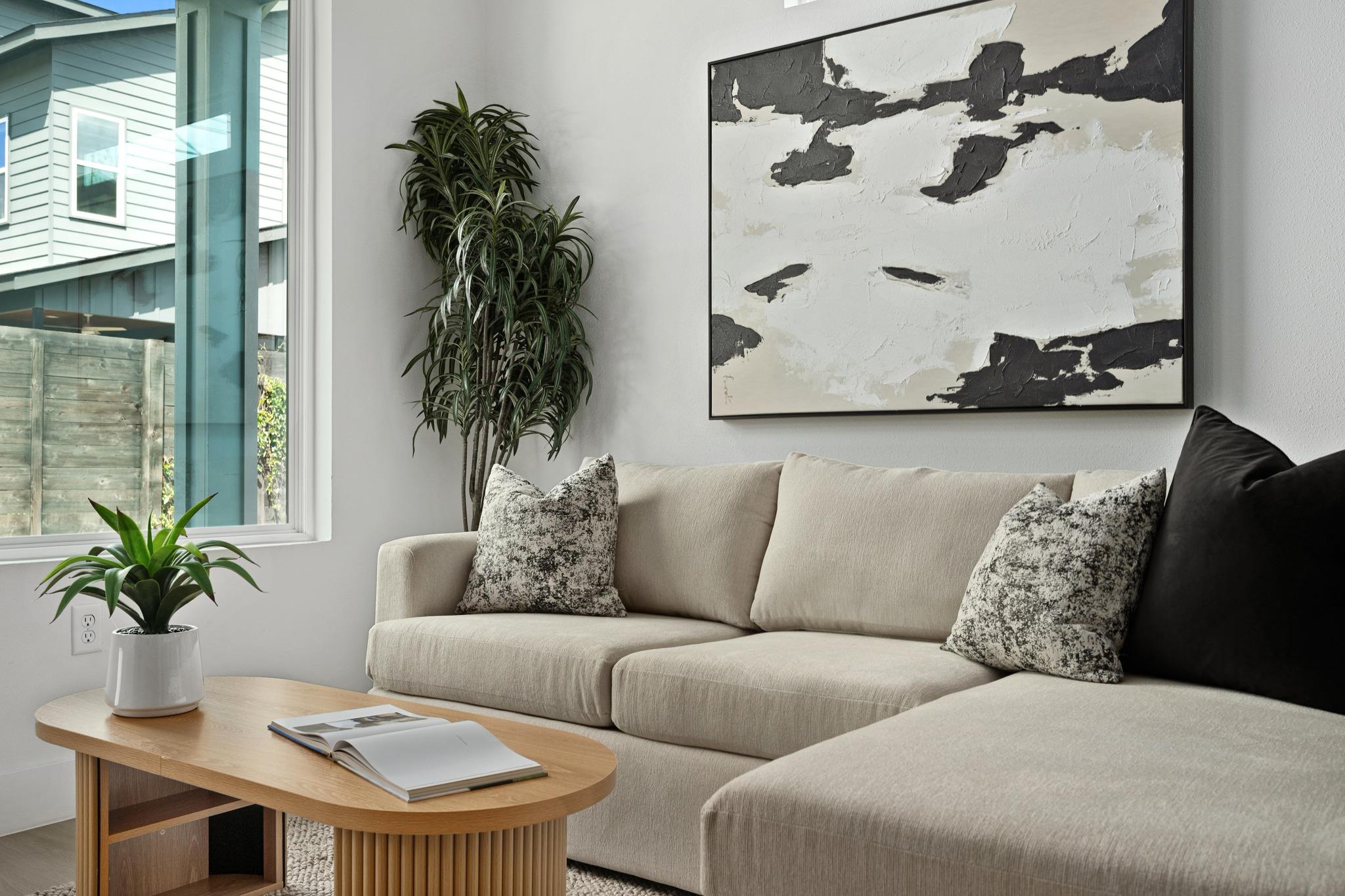 Living room with a cream sectional, oversized abstract artwork, houseplants, and an oval wood coffee table.