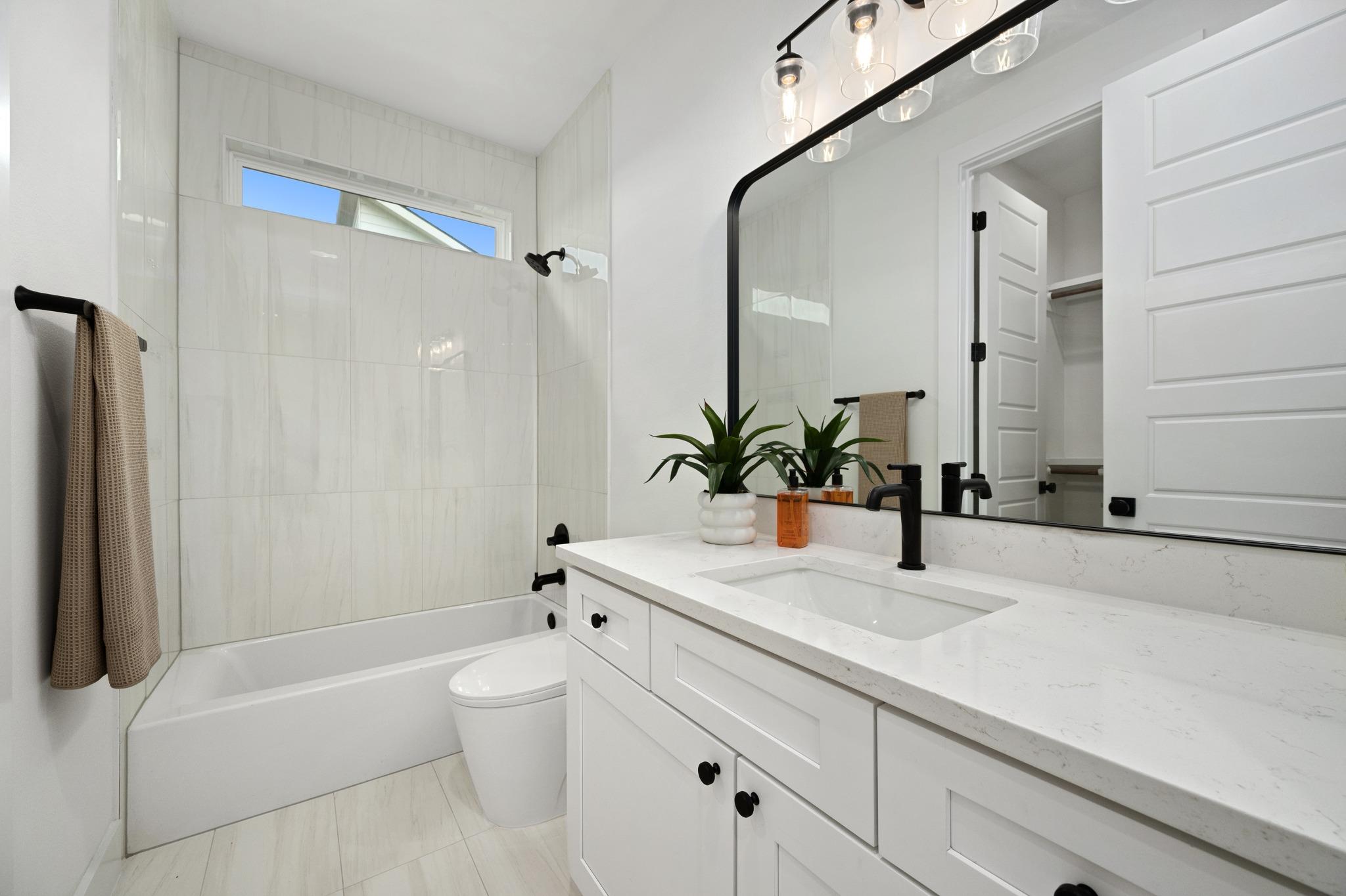 Bright bathroom with a tiled tub and shower, white vanity, black fixtures, and large mirror.