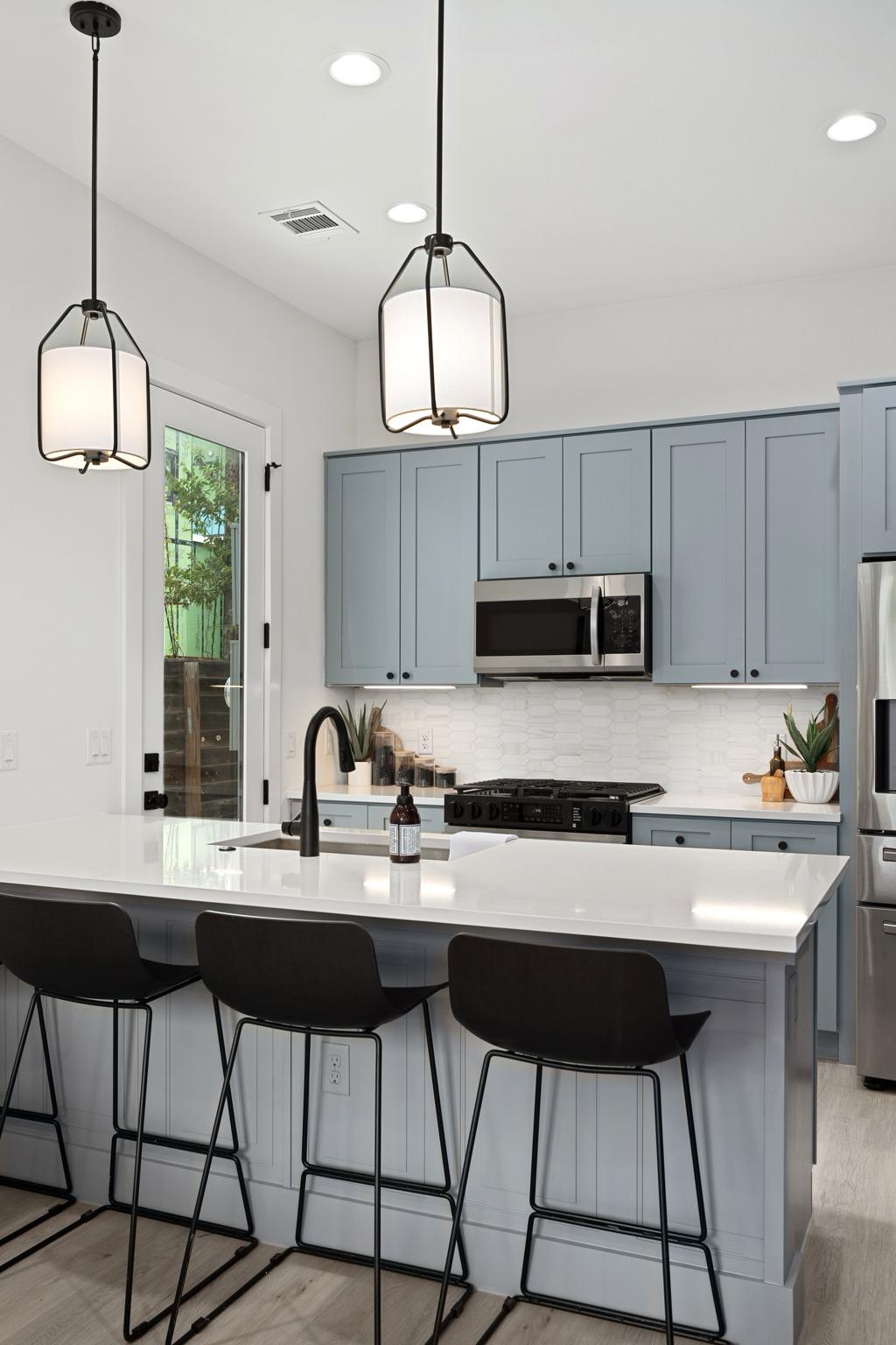 Kitchen with blue-gray cabinets, a white island, black faucet, and three bar stools.