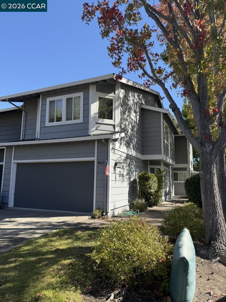 Two-story gray house with an attached garage and a mature tree shading the front.
