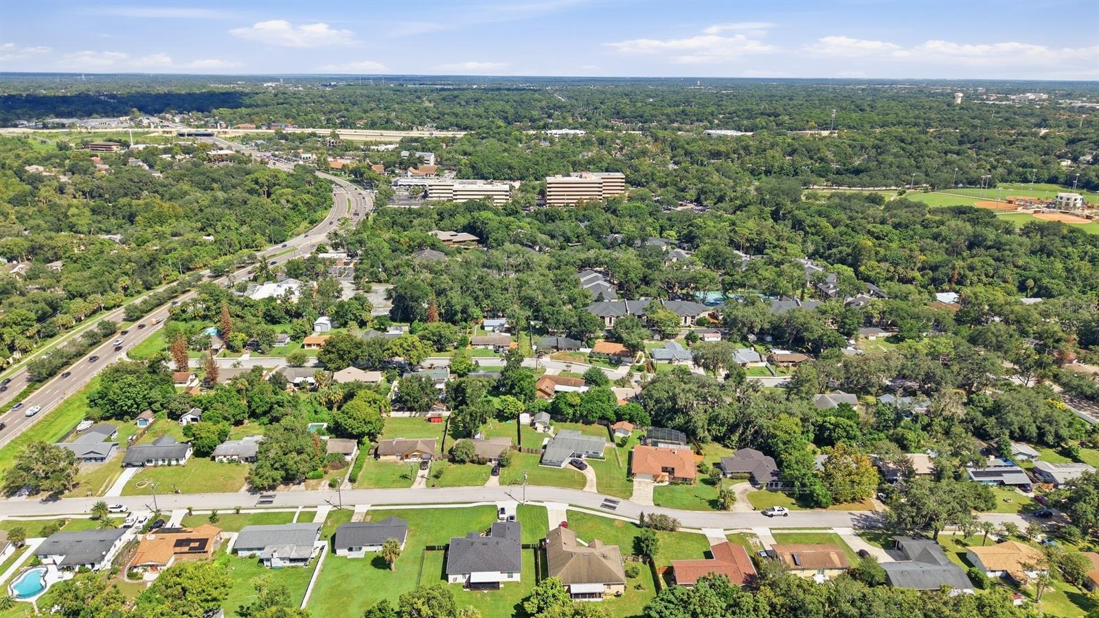 Aerial view of a leafy suburban neighborhood, with homes, a curving road, and sports fields.