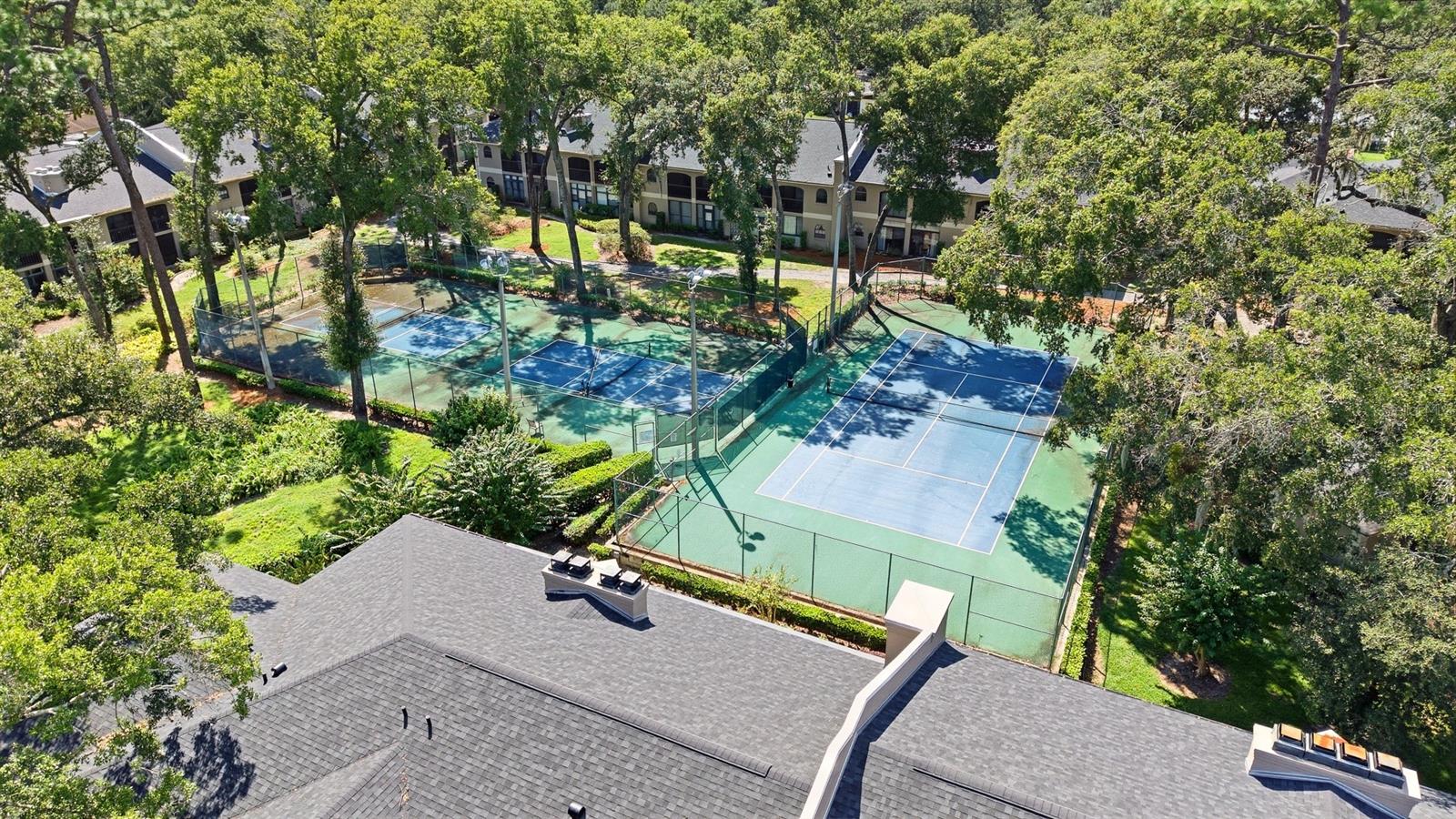Aerial view of fenced tennis courts among mature trees beside condominium buildings.