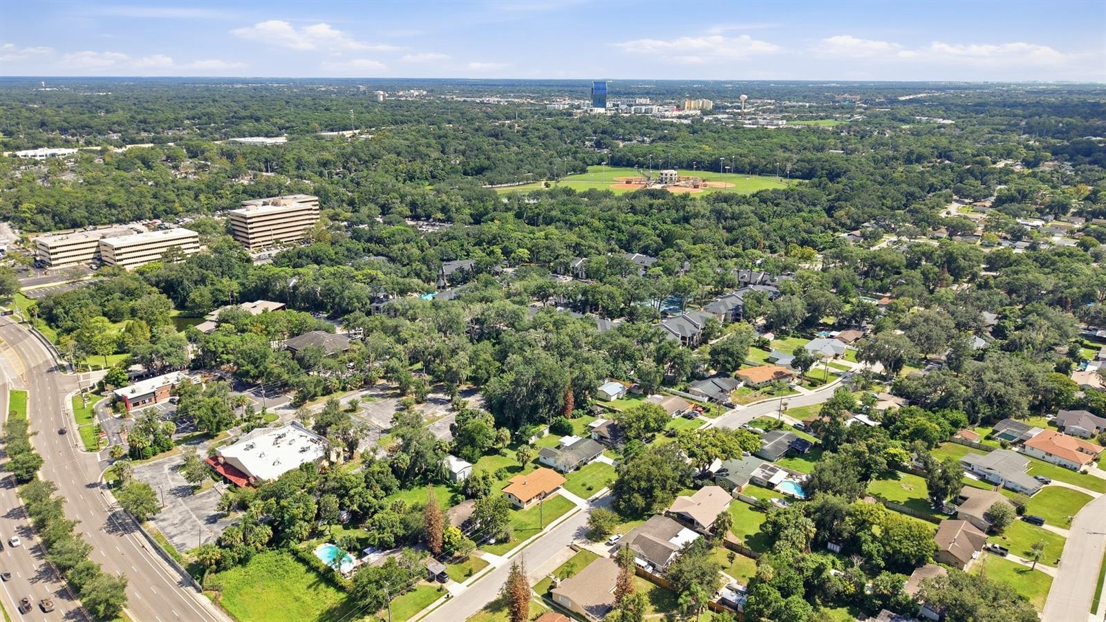 Aerial view of a tree-lined neighborhood with a sports field and office buildings in the distance.