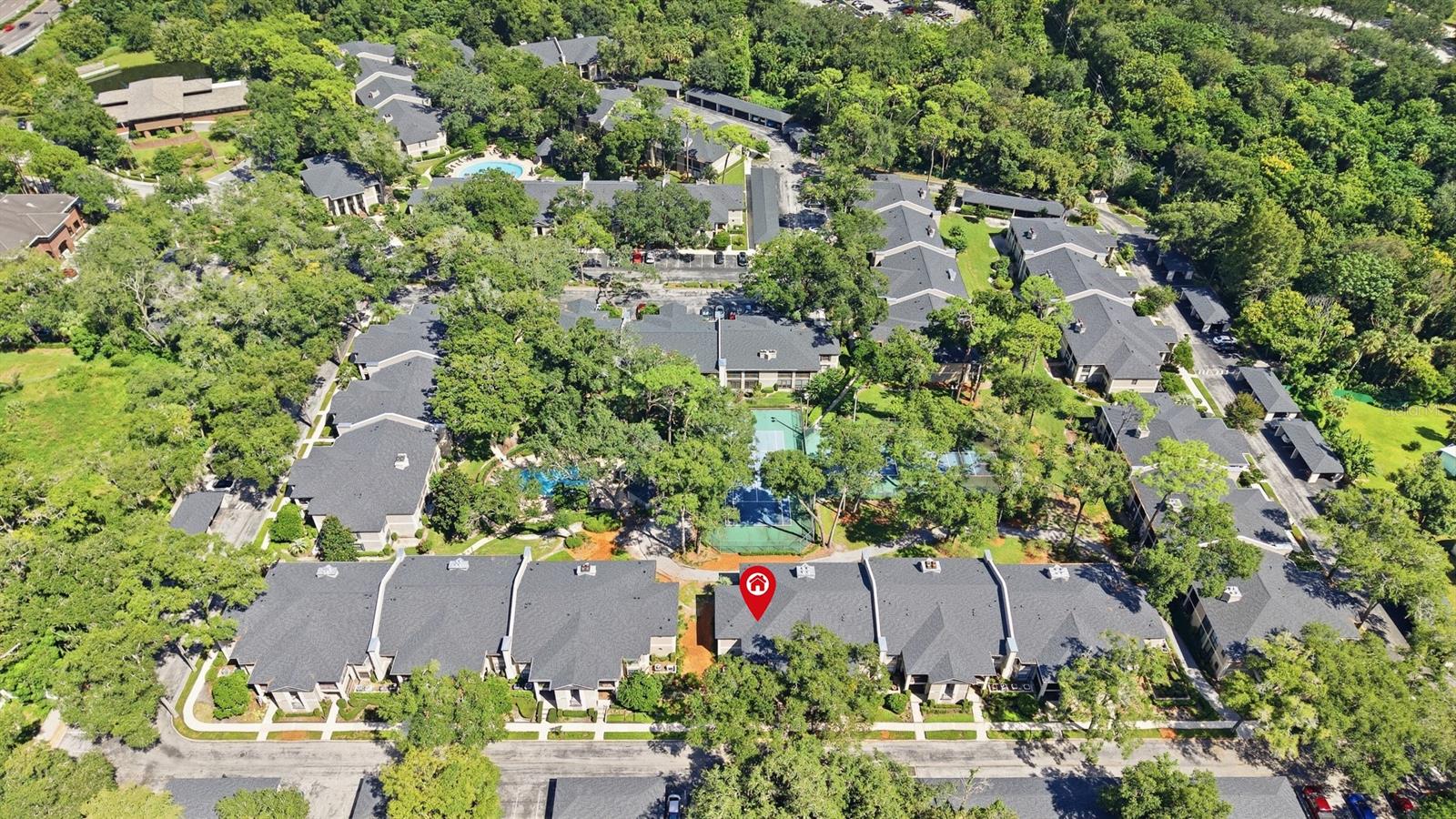 Aerial view of the marked condominium unit among tree-lined homes, with tennis courts and a pool nearby.