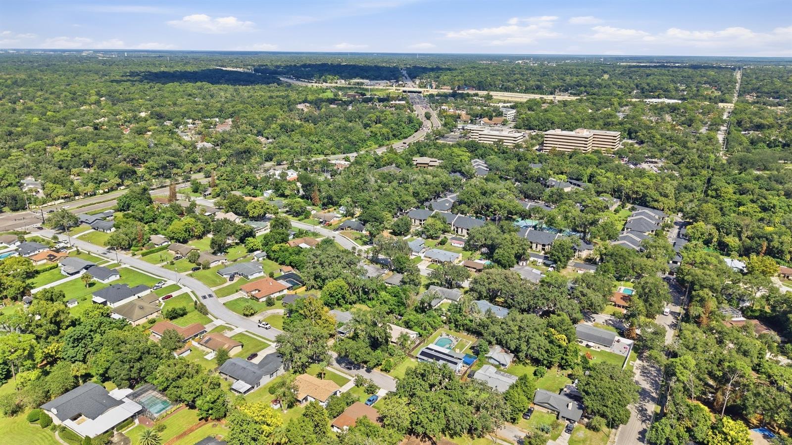 Aerial view of a leafy neighborhood with homes, tree-lined streets, and distant office buildings.