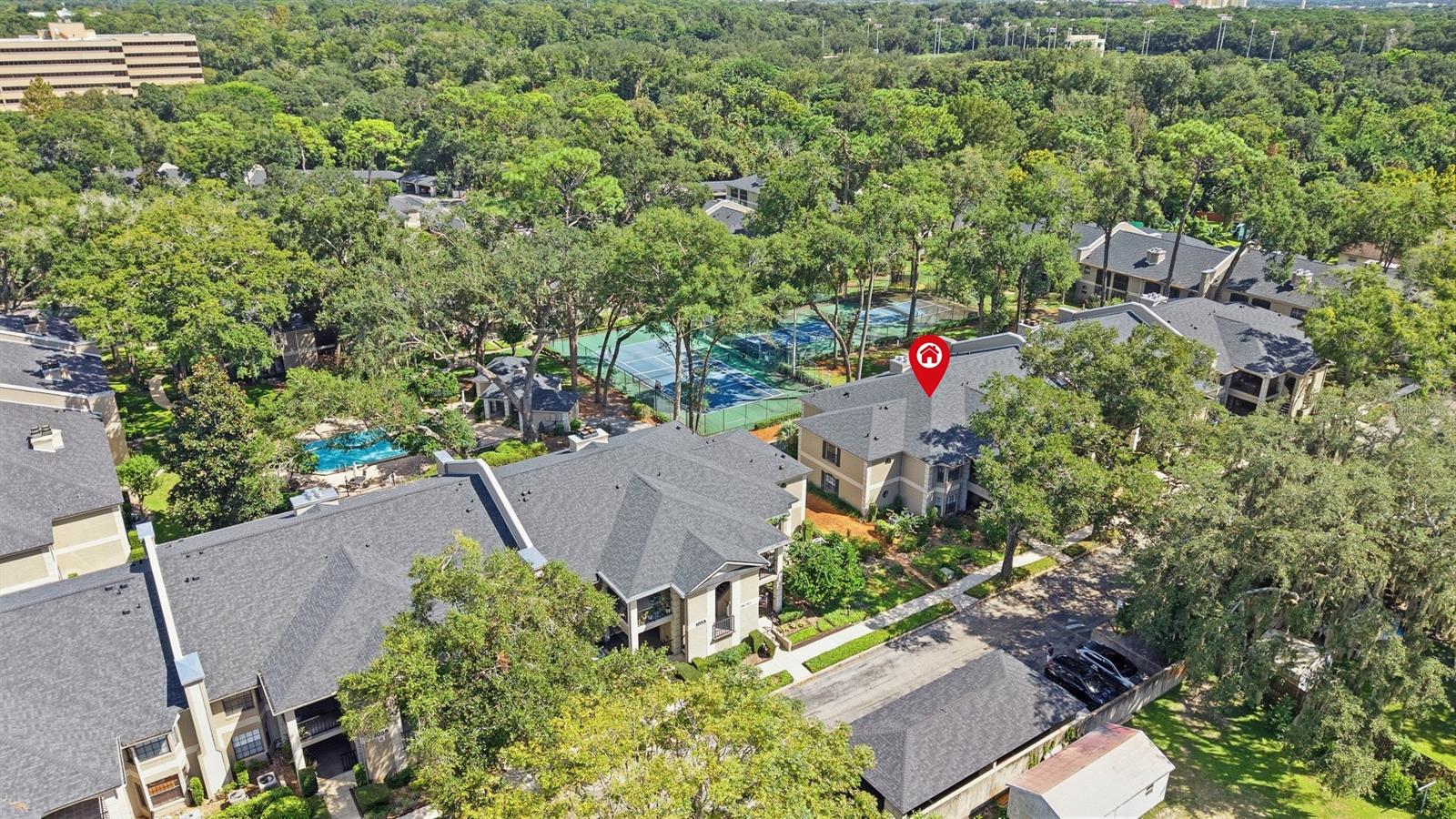 Aerial view of an apartment complex with a pool, tennis courts, and a marked building.