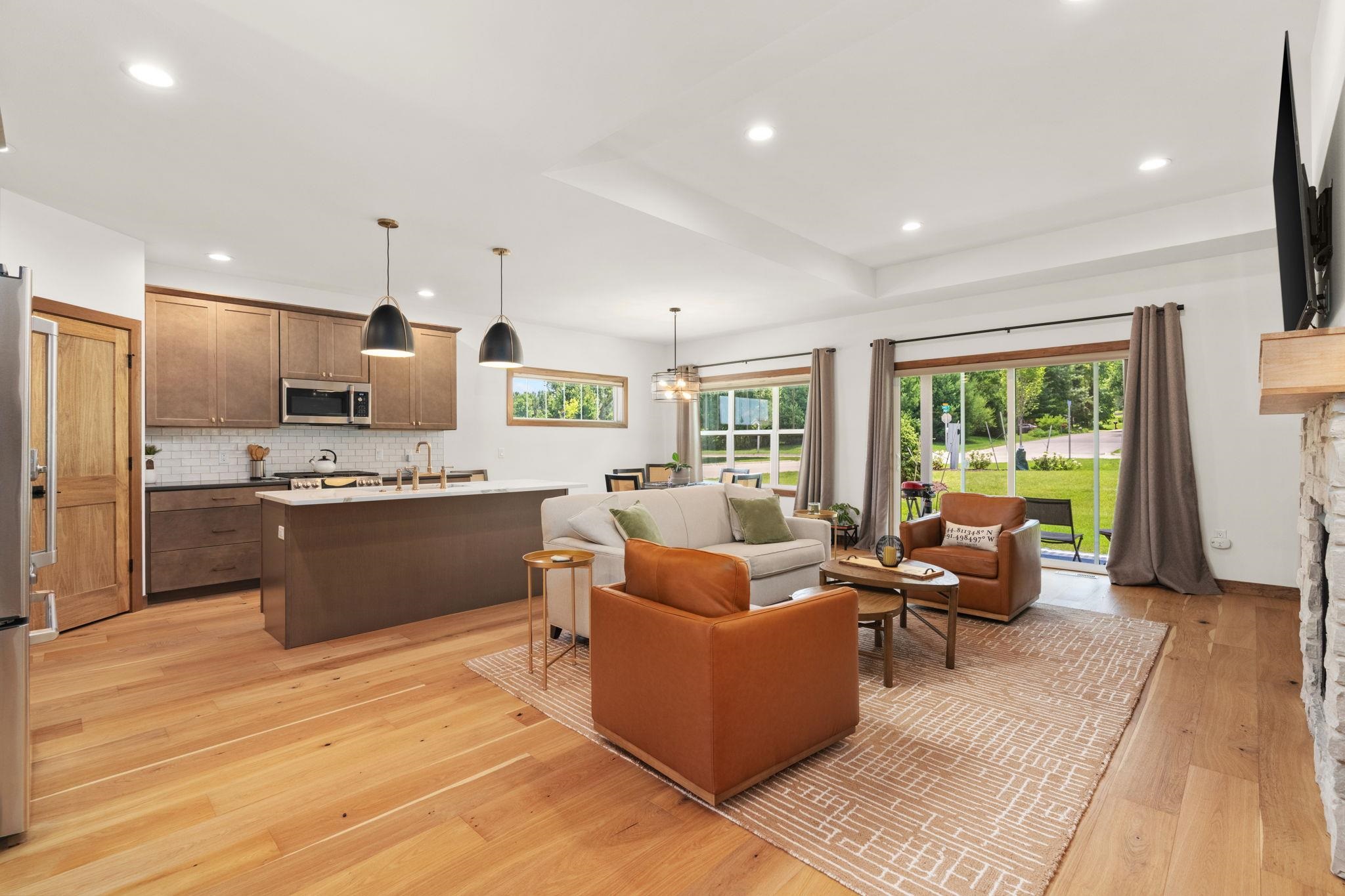 Open-plan kitchen and living room with a large island, warm wood floors, and sliding doors to the yard.