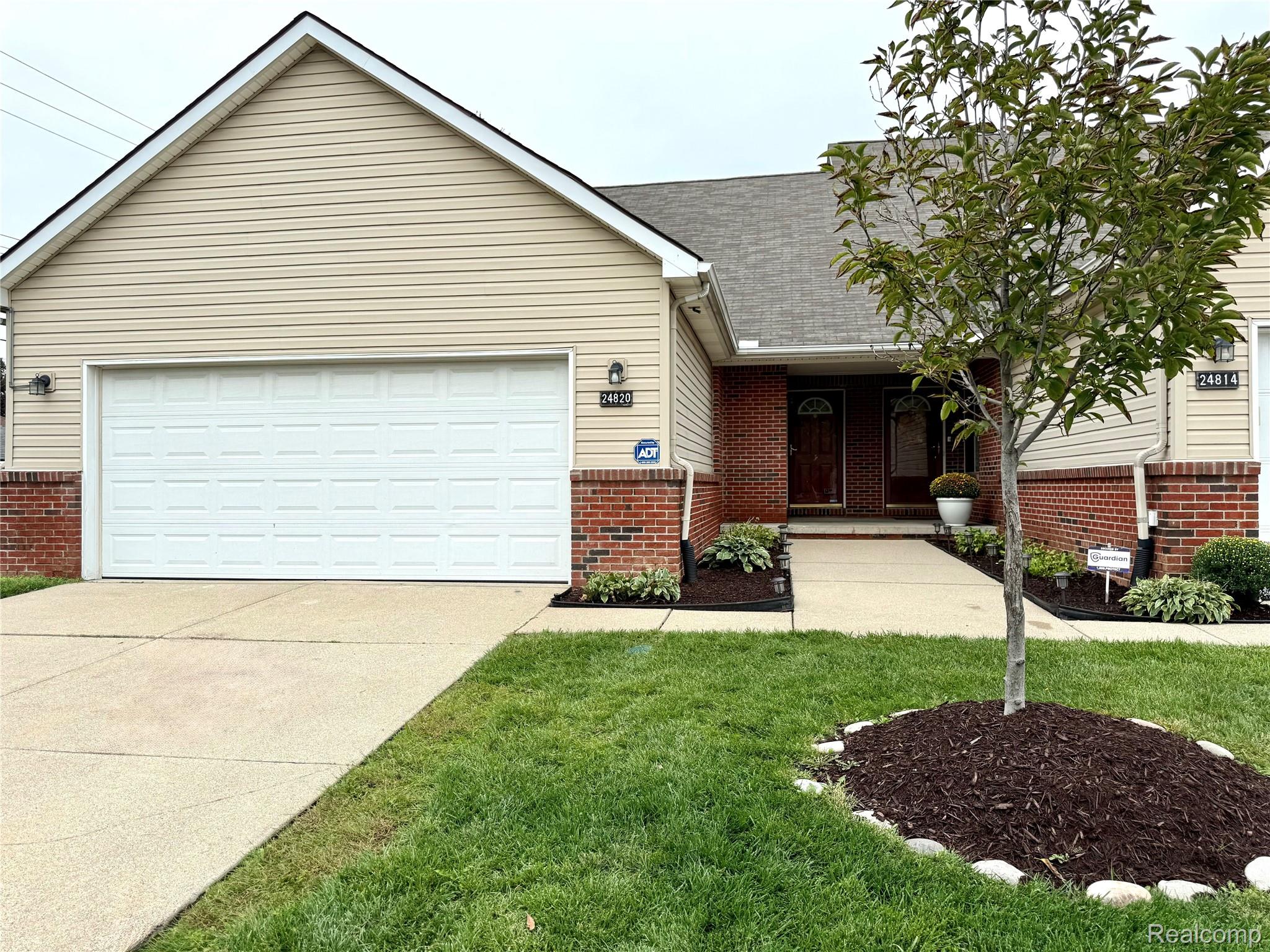 Beige-sided home with brick accents, a white double garage door, and a landscaped front lawn.