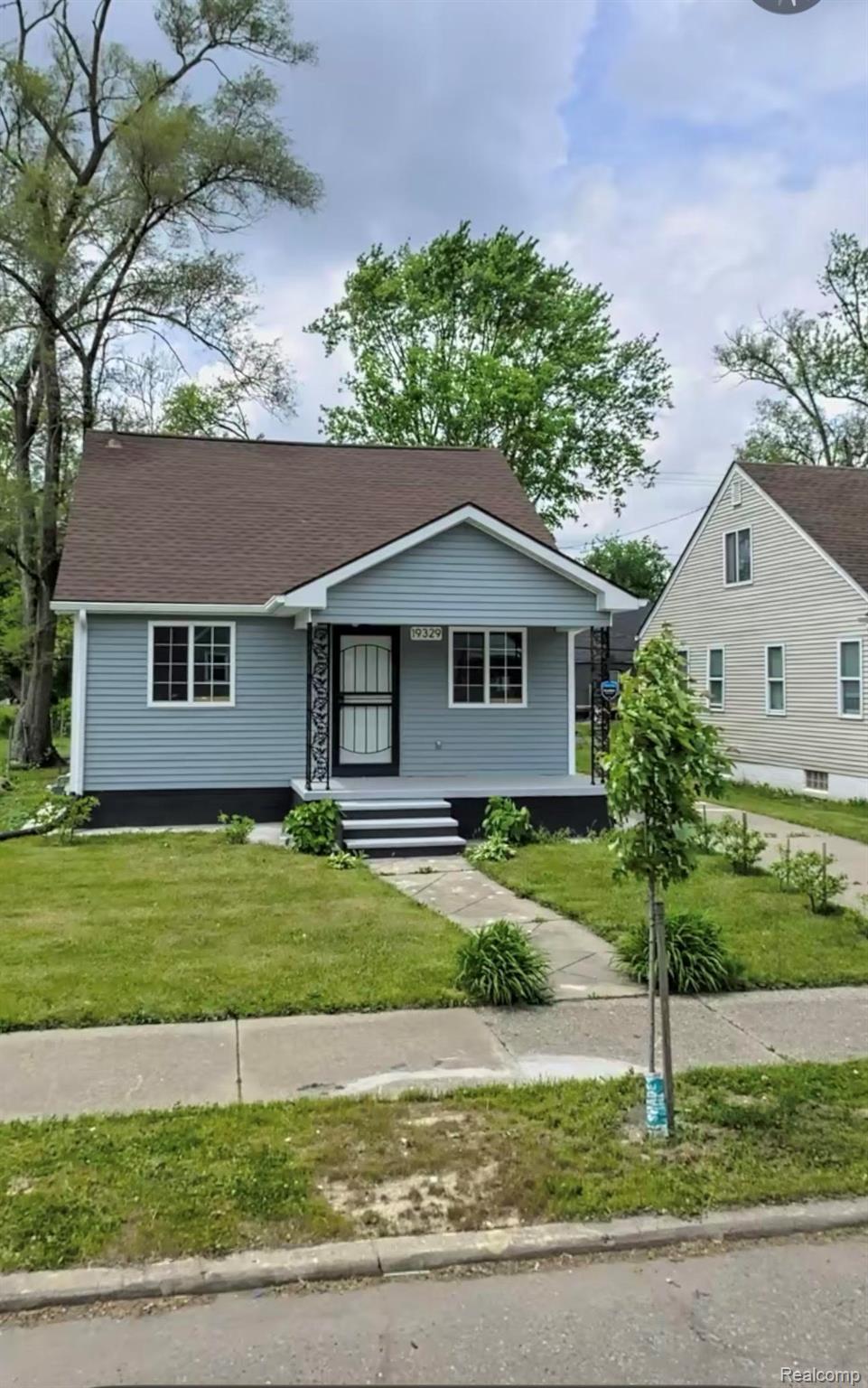 Blue-gray single-story house with white trim, dark front door, and a landscaped front lawn.