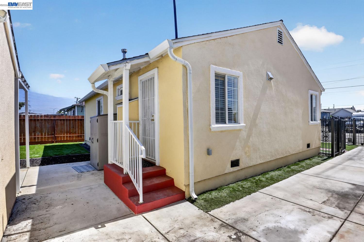 Yellow stucco home with red entry steps and a small fenced lawn.