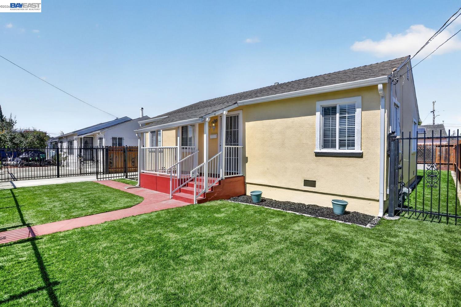 Yellow single-story house with red front steps, a curved walkway, and a fenced lawn.
