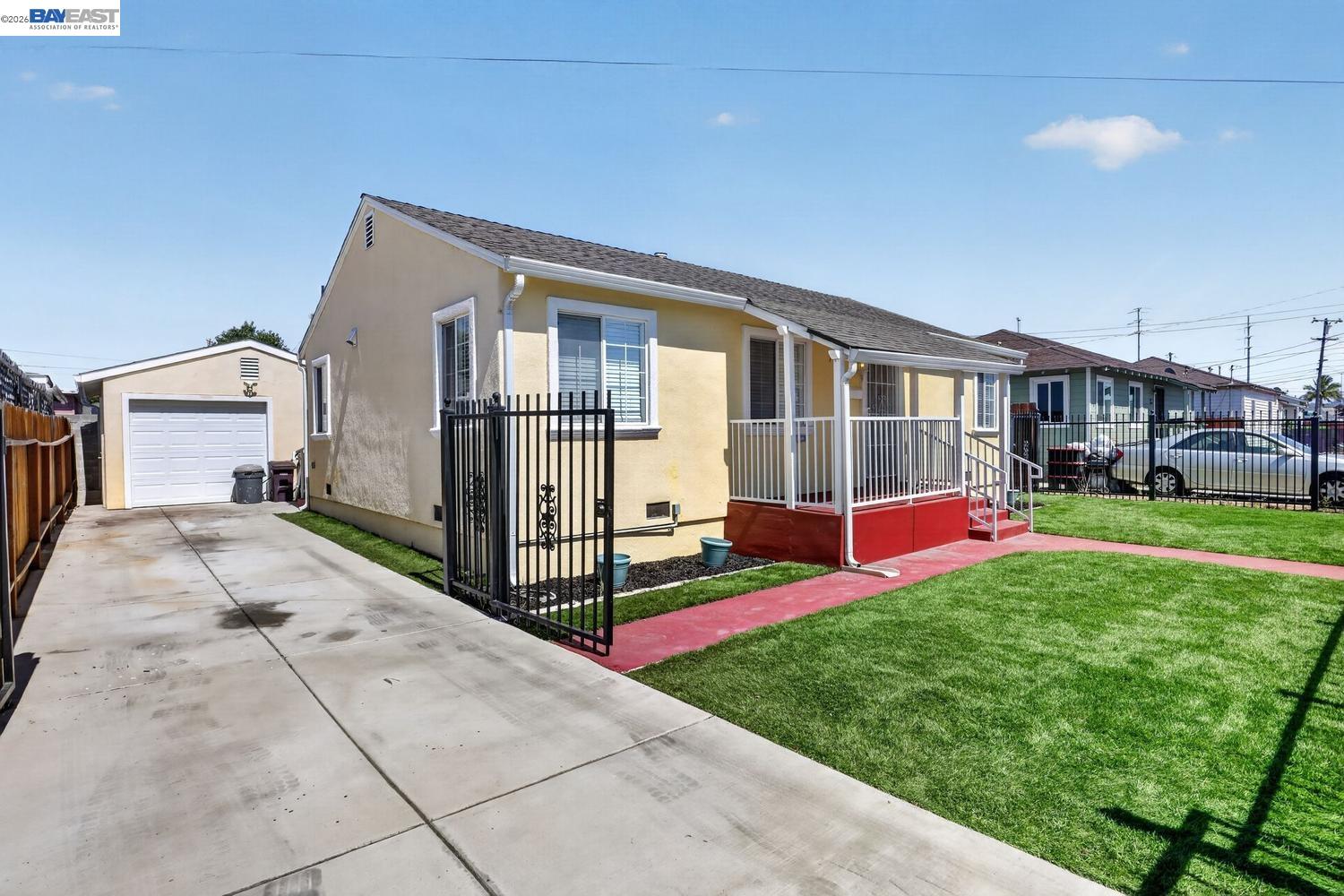 Single-story beige home with red porch, fenced lawn, long driveway, and detached garage.