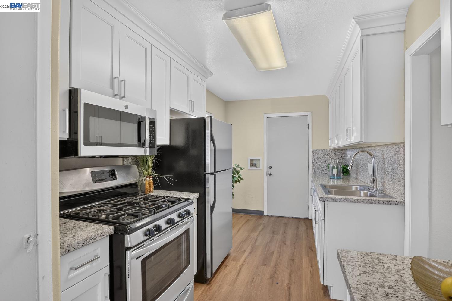 Galley kitchen with white cabinets, speckled stone counters, stainless gas range, and black refrigerator.