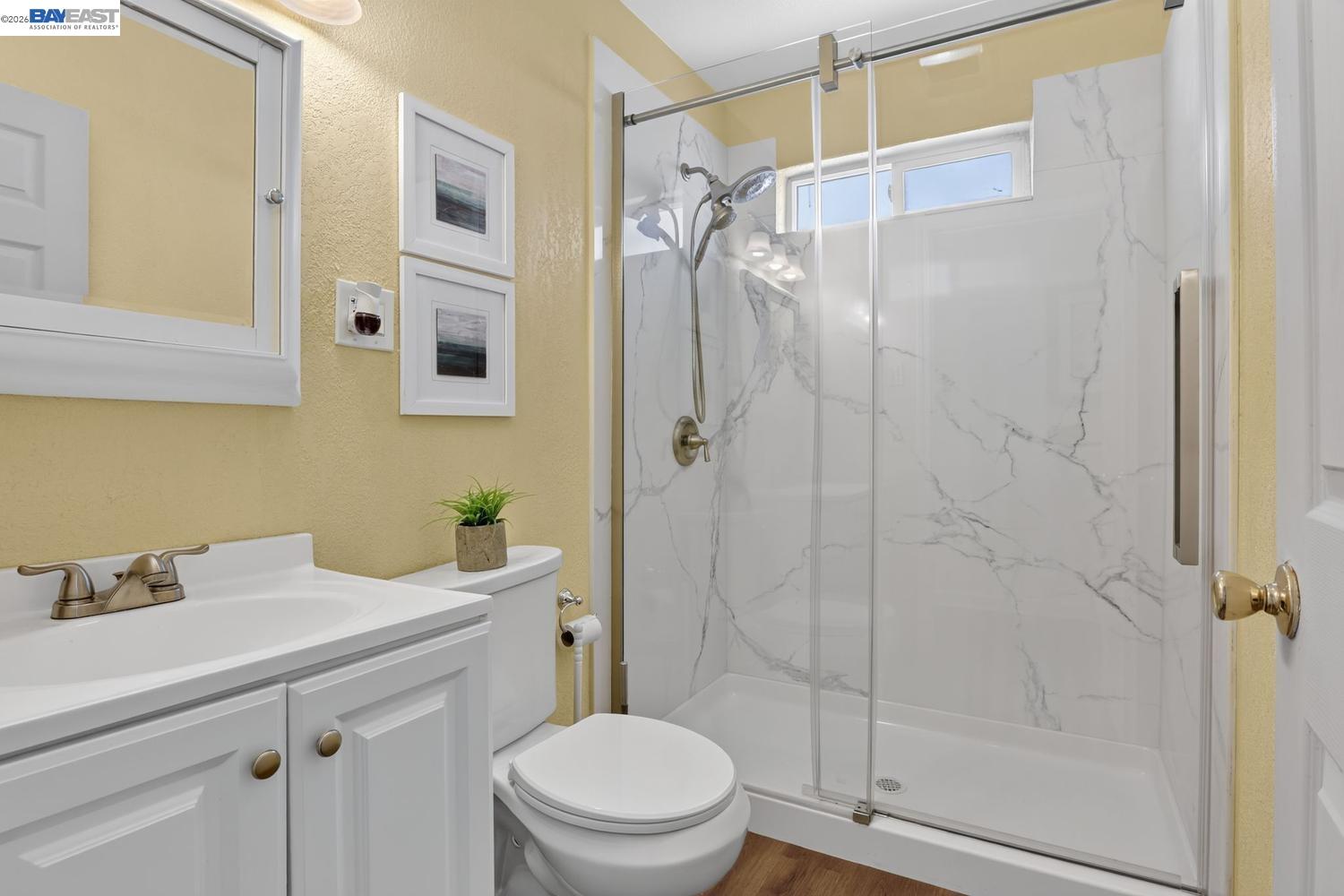 Bathroom with a marble-look glass shower, white vanity, and toilet.